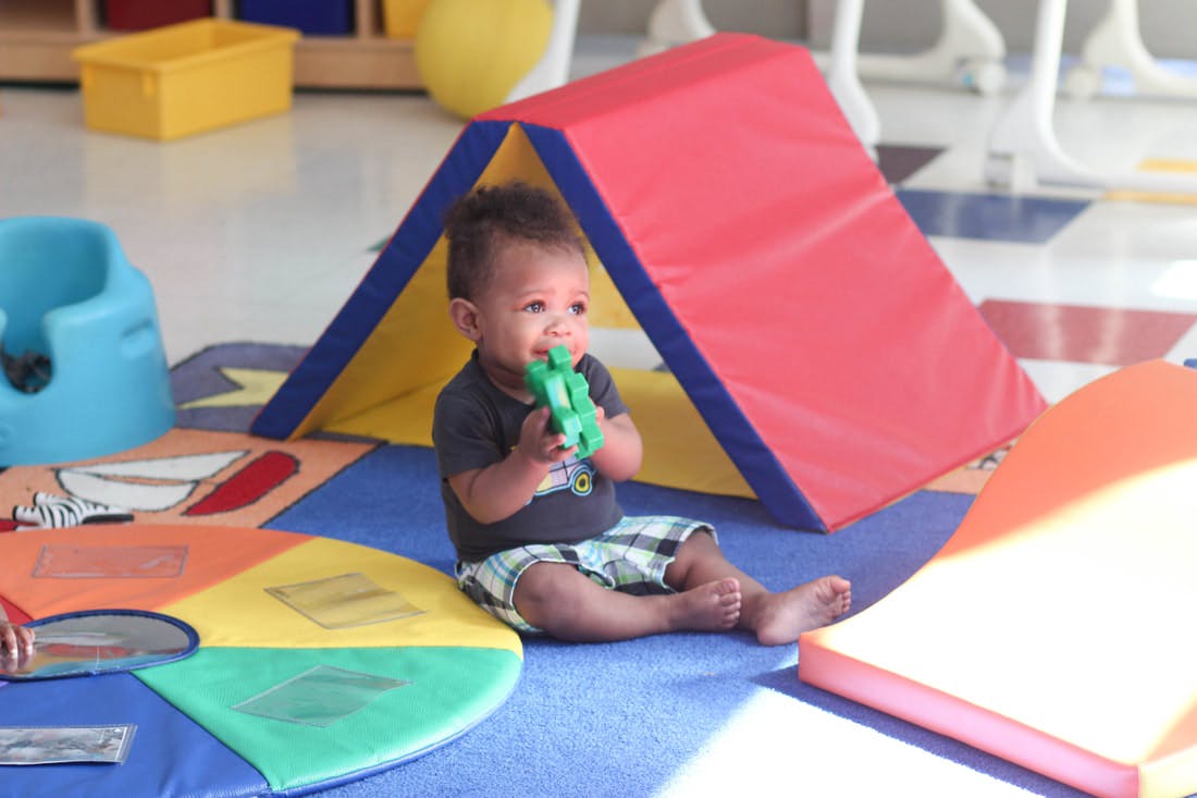 Child sitting on floor with toy in front of play mat tent