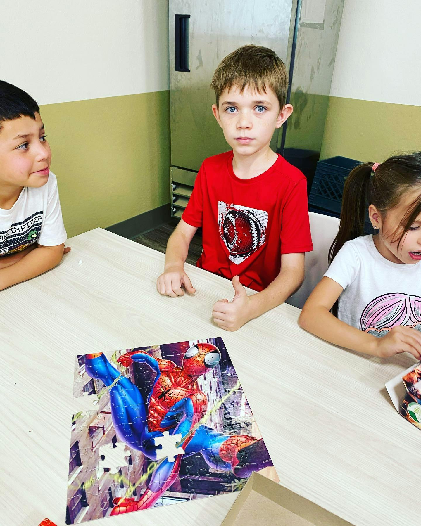 Three children at a table with a partially completed Spider-Man puzzle