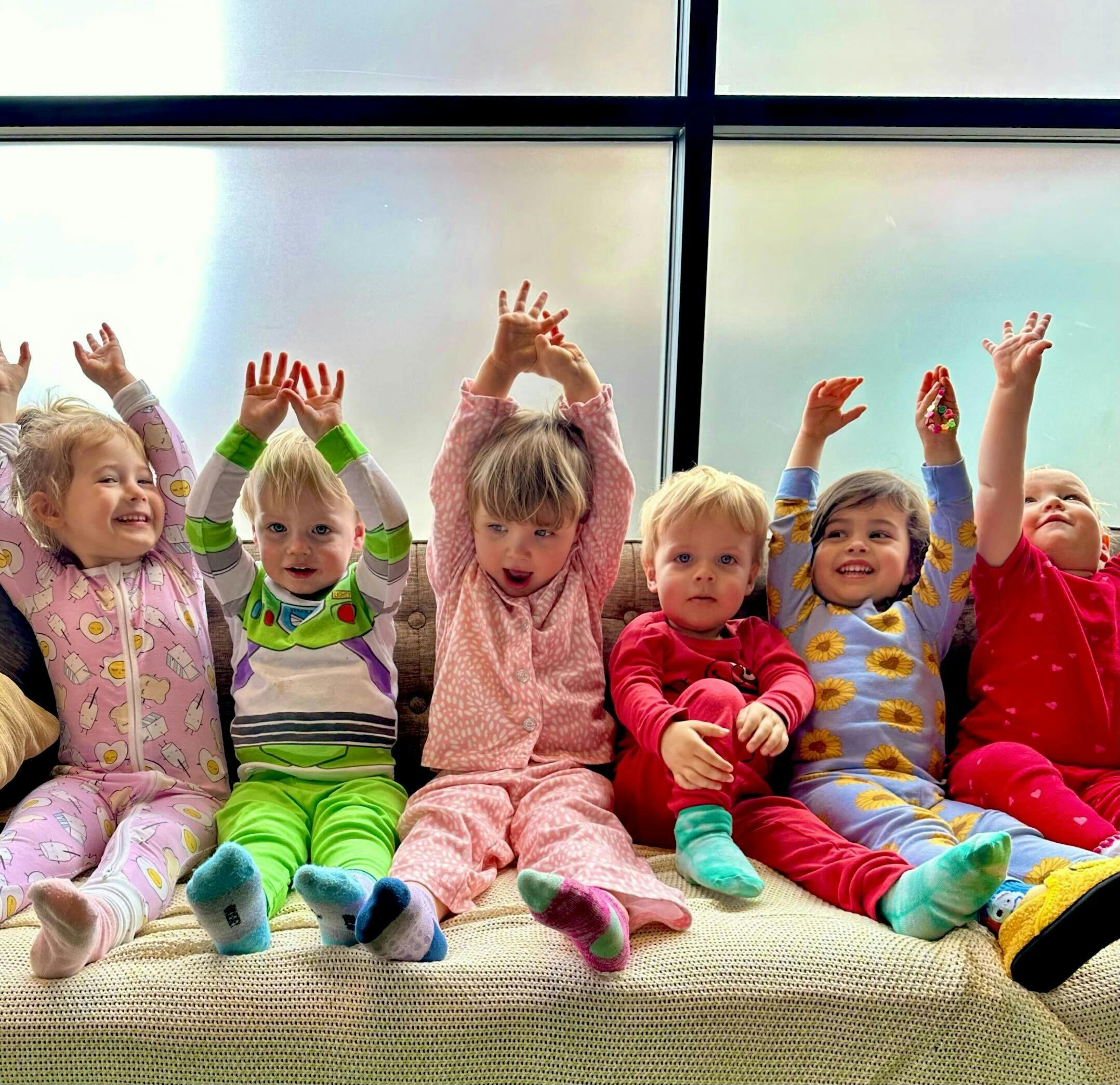Group of children sitting on a couch with their arms raised