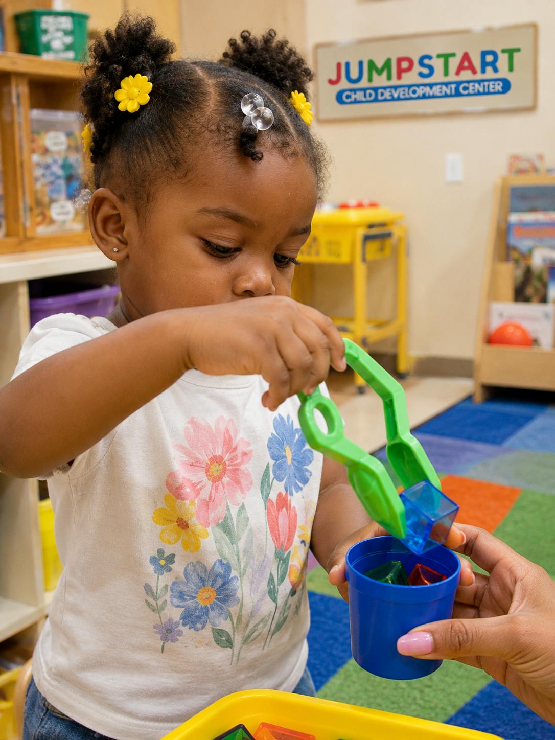 Child using green toy tweezers to place a blue block into a cup