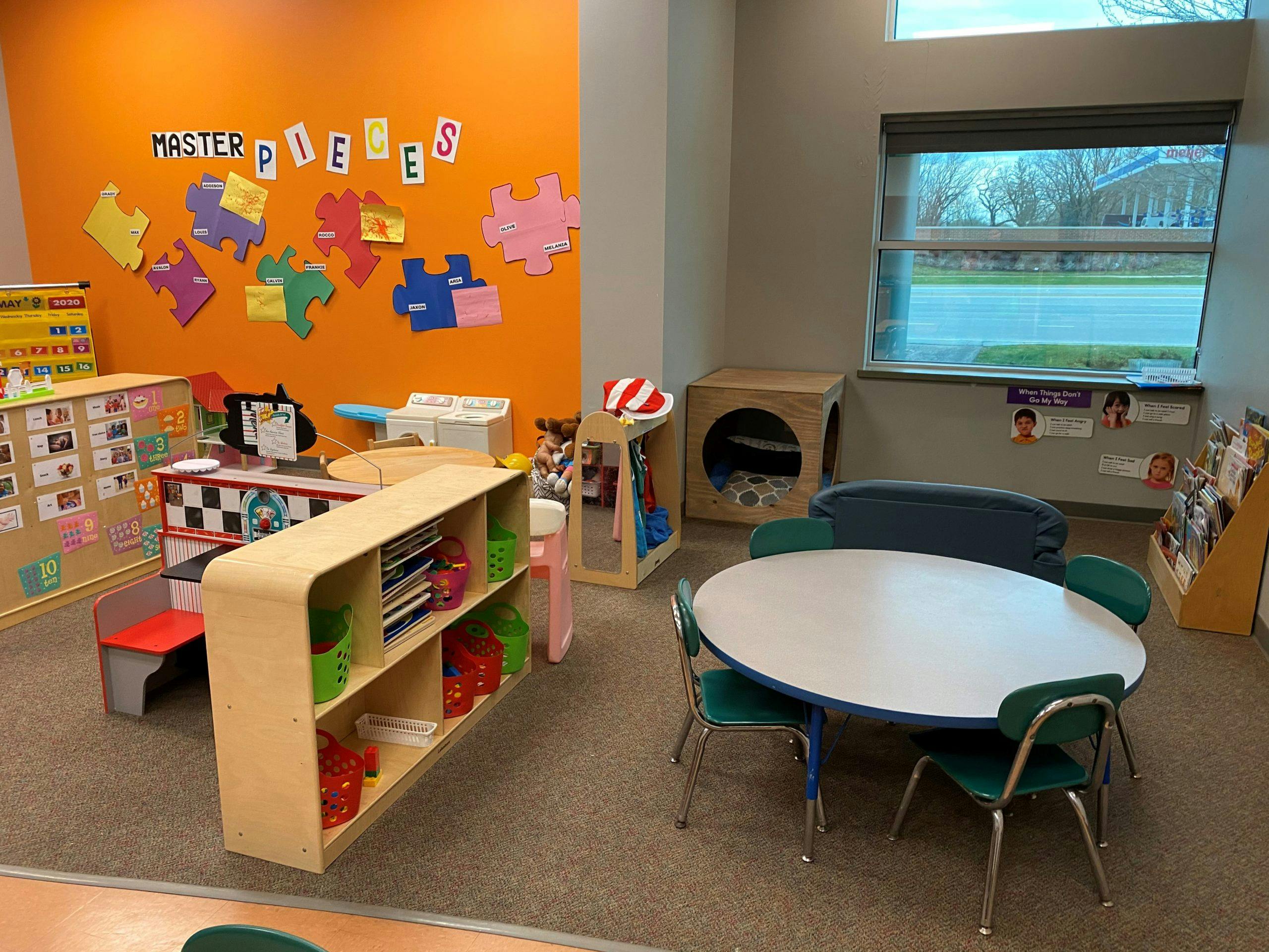 Classroom with an orange wall, tables, chairs, and shelves