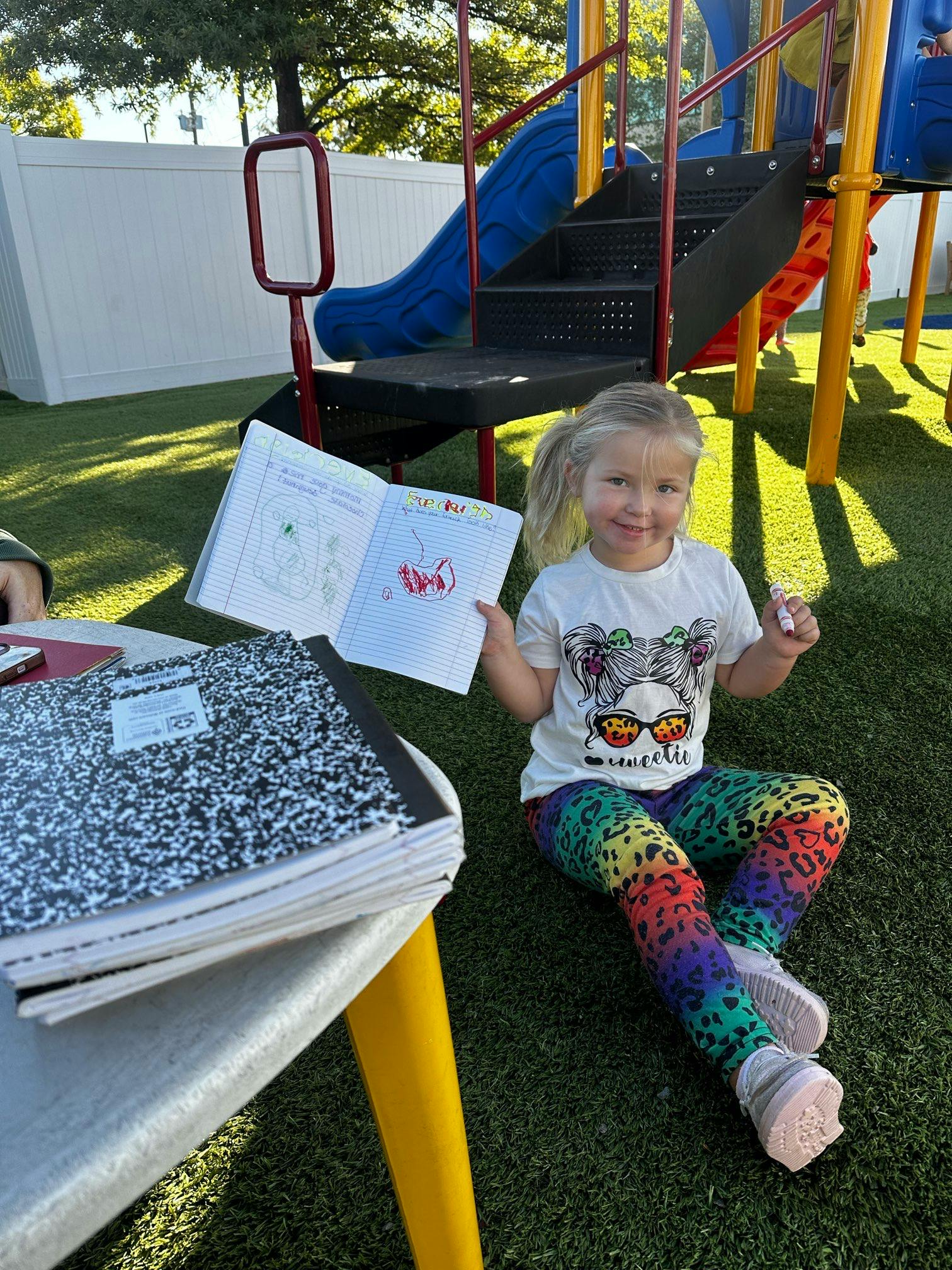 Child sitting on grass holding an open book with drawings