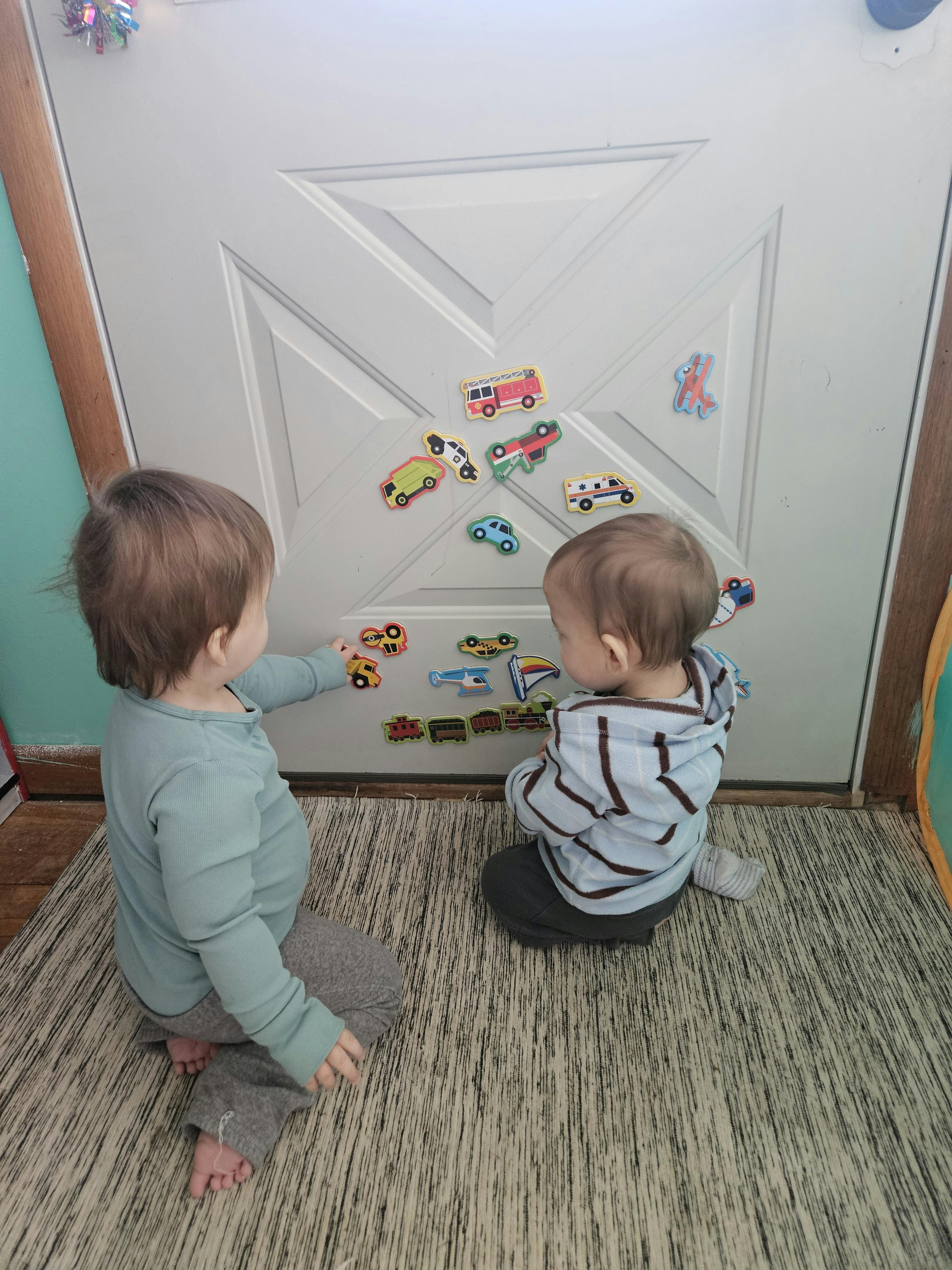 Two young children playing with magnetic vehicle shapes on a white door