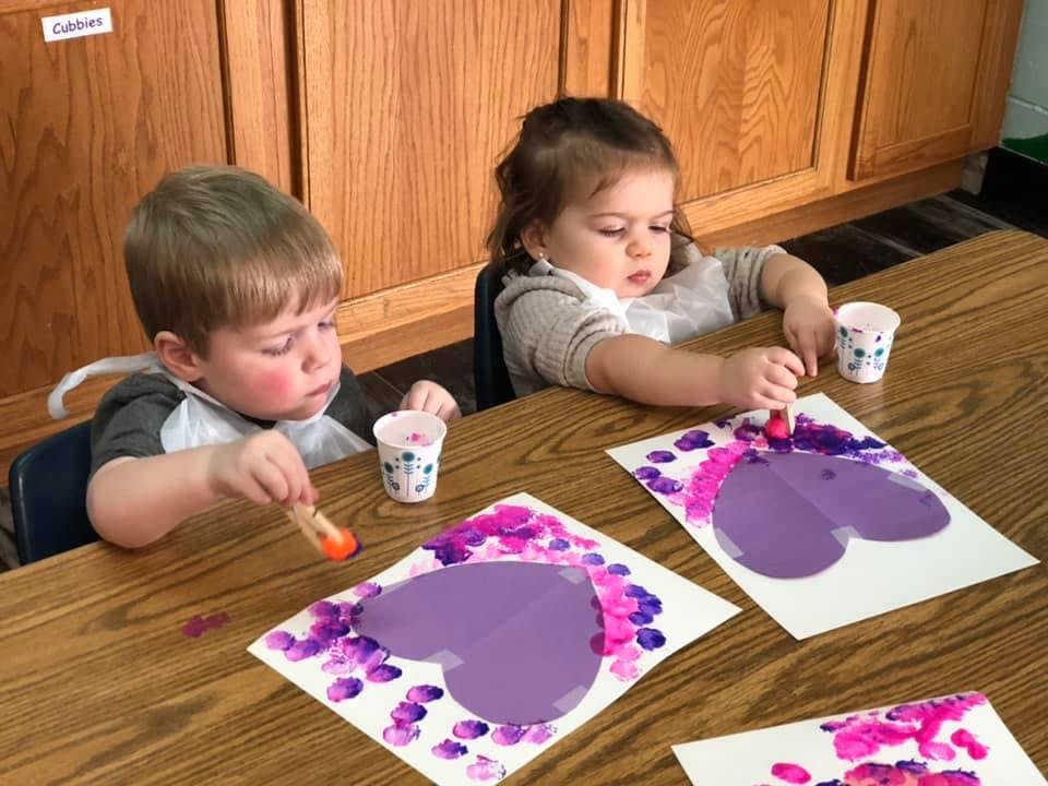 Two children painting heart shapes on paper at a table