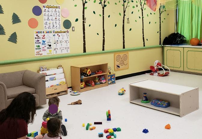Adult and two children playing with blocks on the floor in a classroom