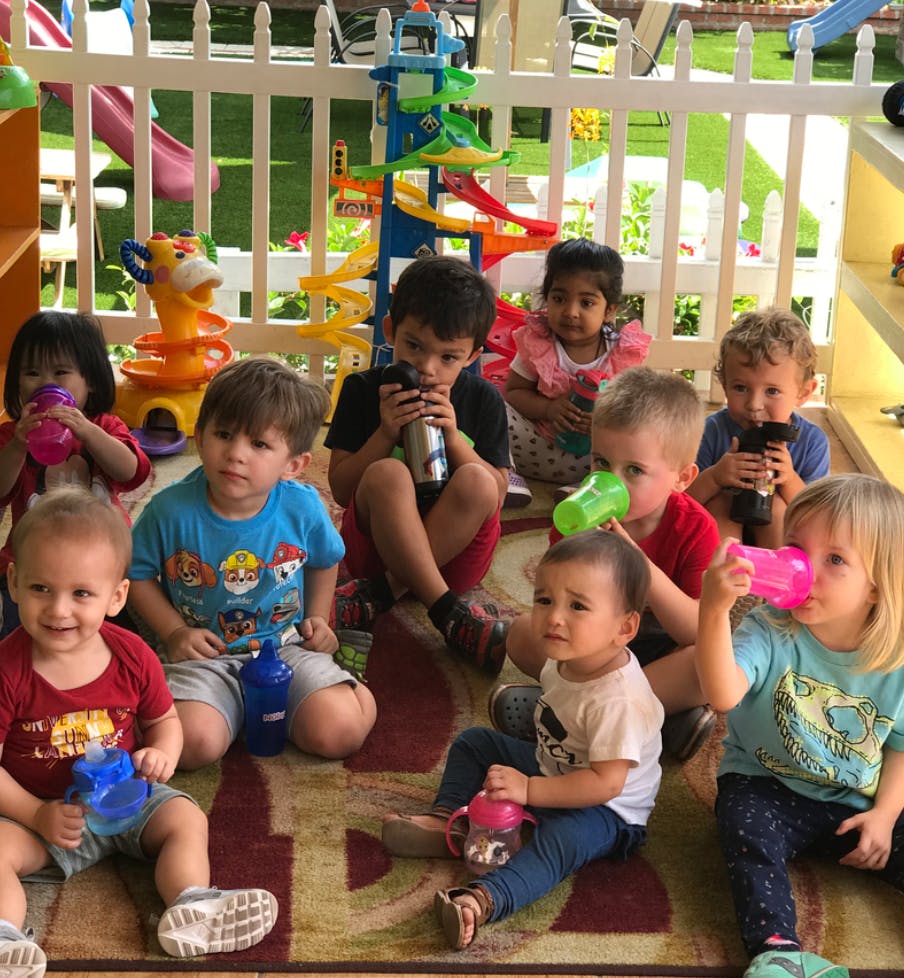 Group of children sitting on a rug with sippy cups and water bottles