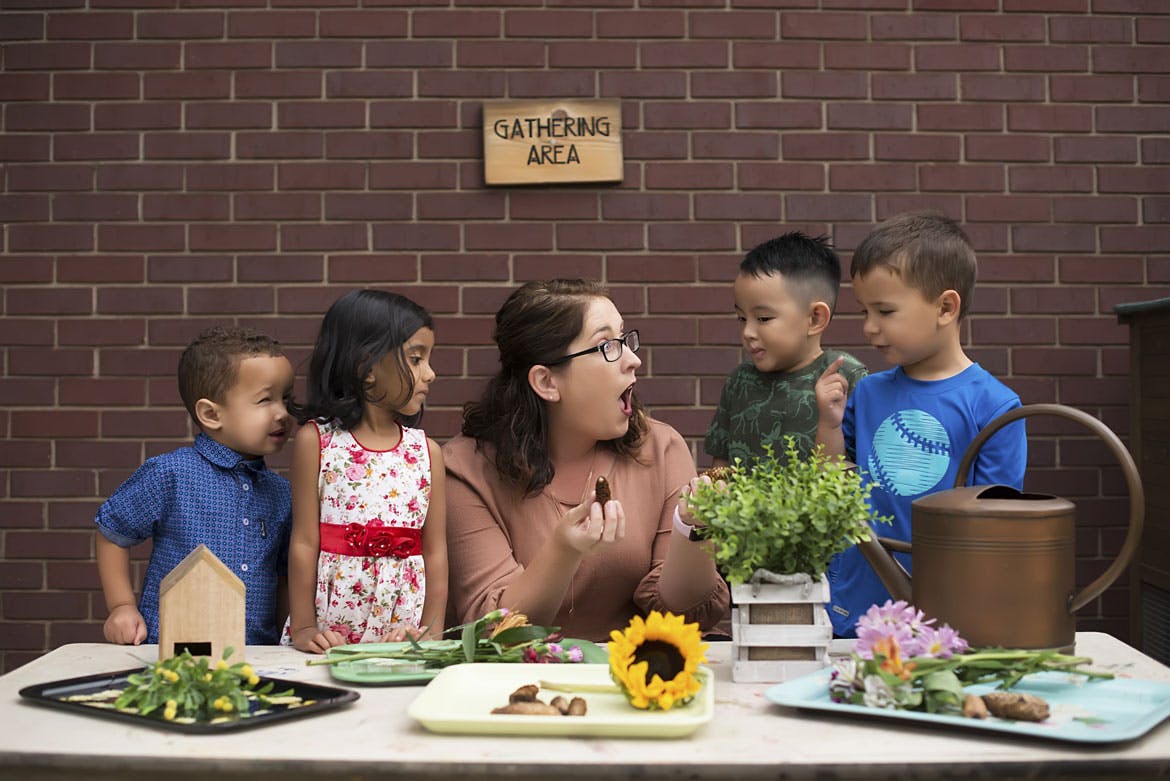 Person with glasses talking to four children at a table with plants
