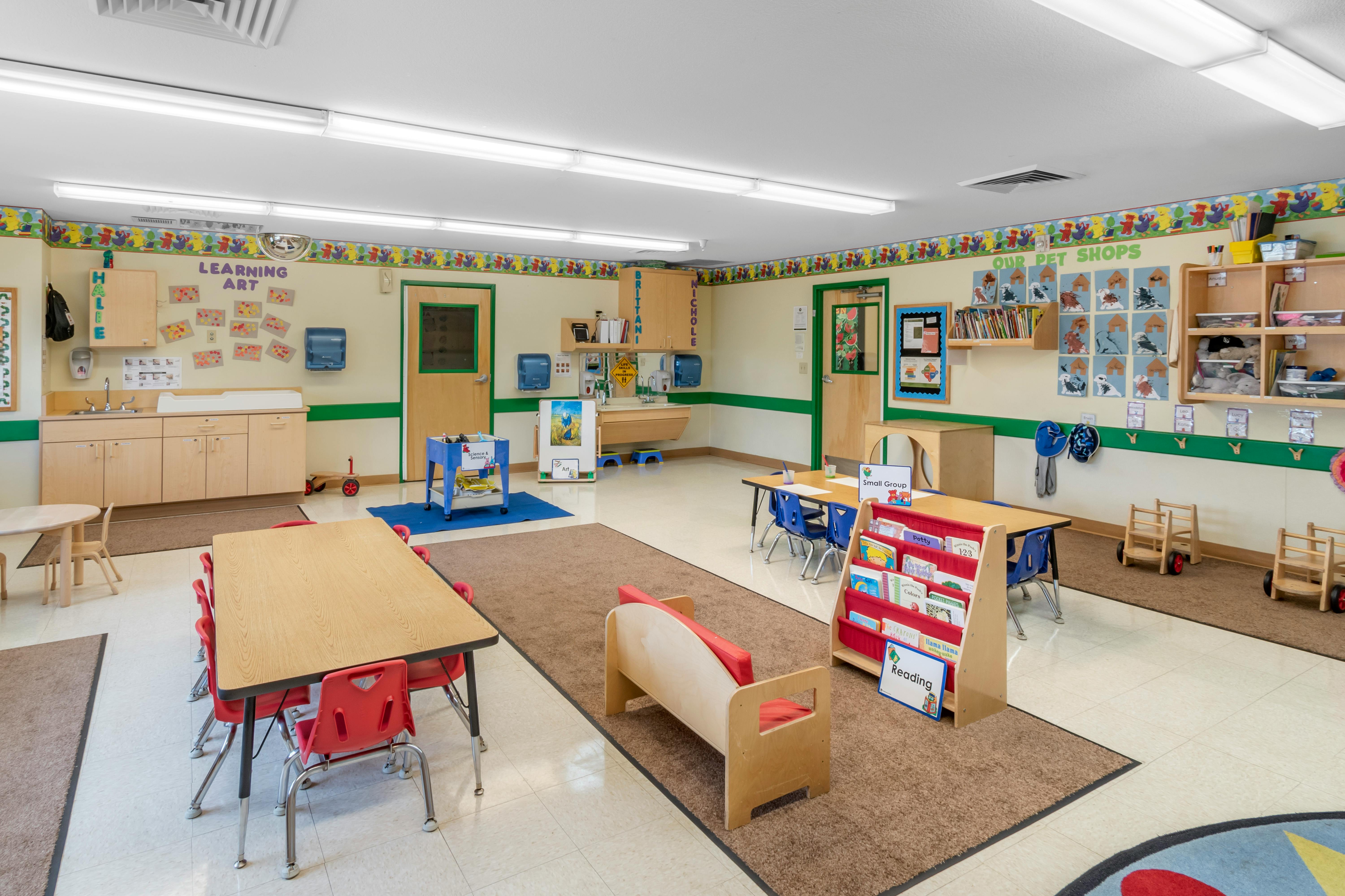 A colorful classroom with small tables and chairs, a sink area, and wall decorations