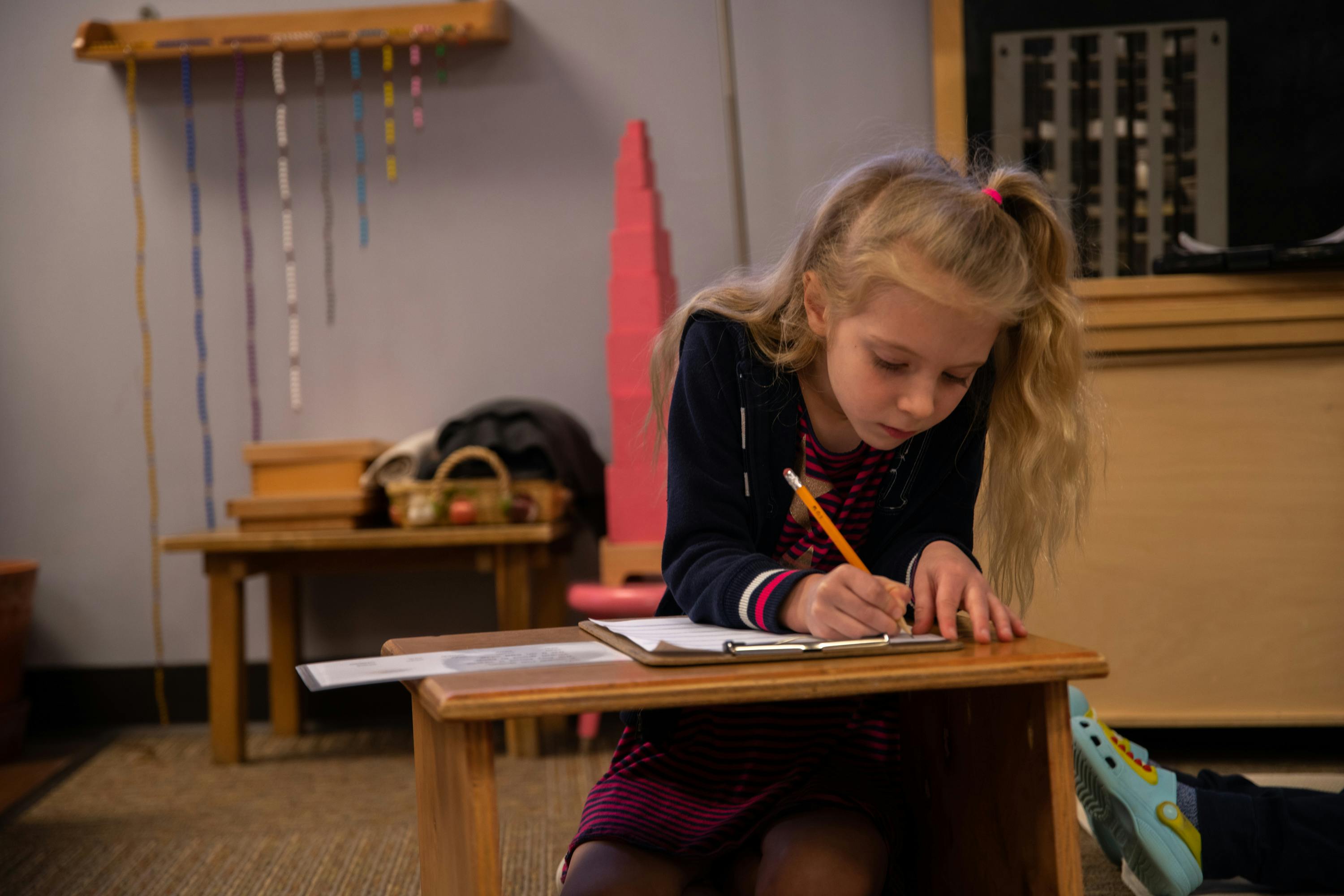 Child writing on a clipboard at a small wooden desk