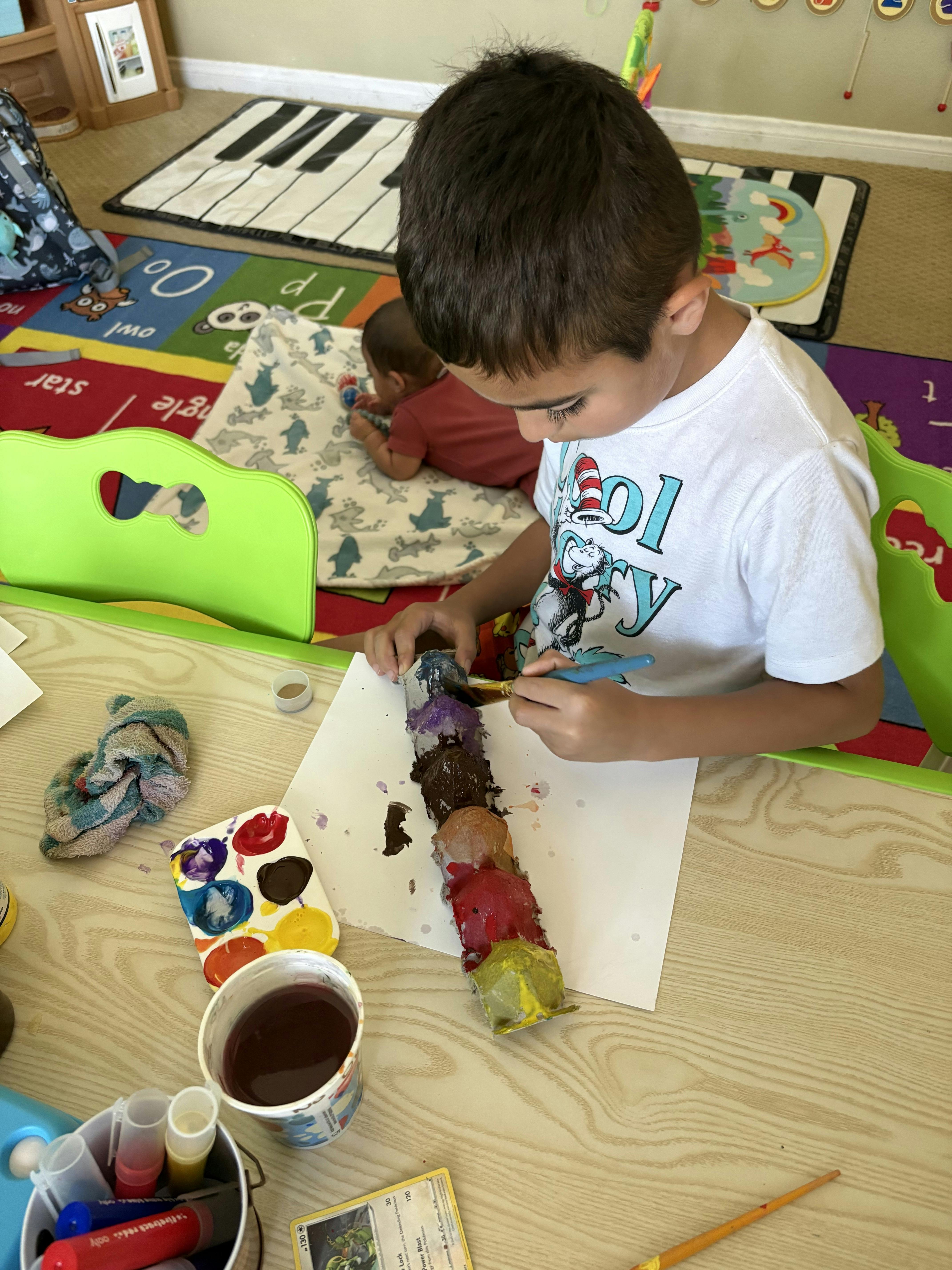 A child painting a cardboard egg carton caterpillar at a table