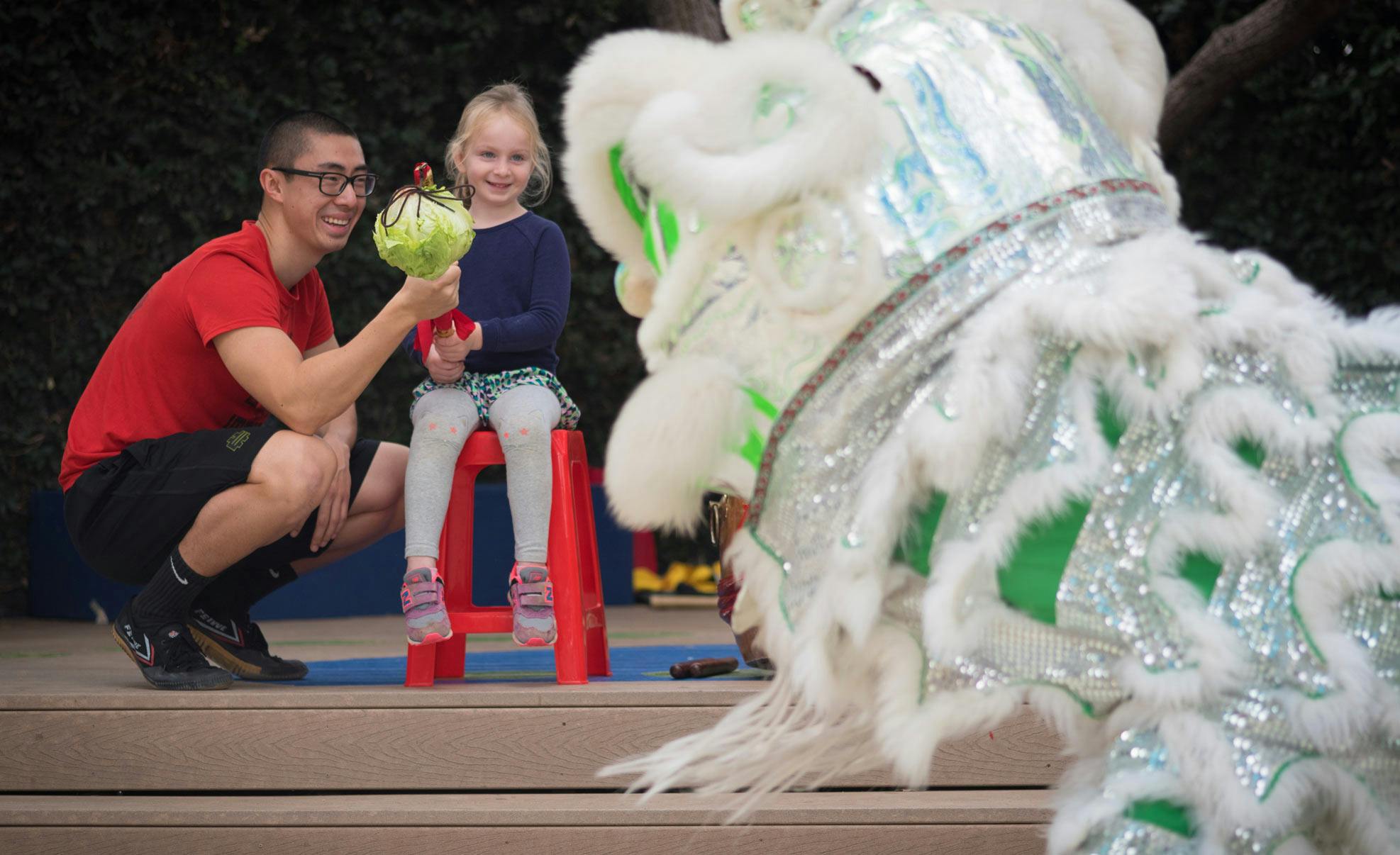 Person and child presenting a head of lettuce to a lion dance costume