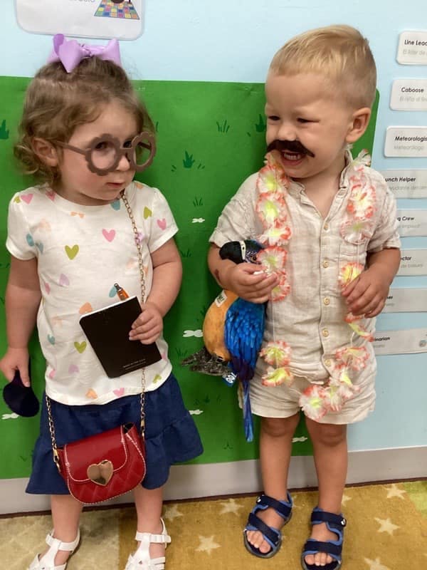 Two children in costumes, one with glasses and a purse, the other with a mustache and parrot