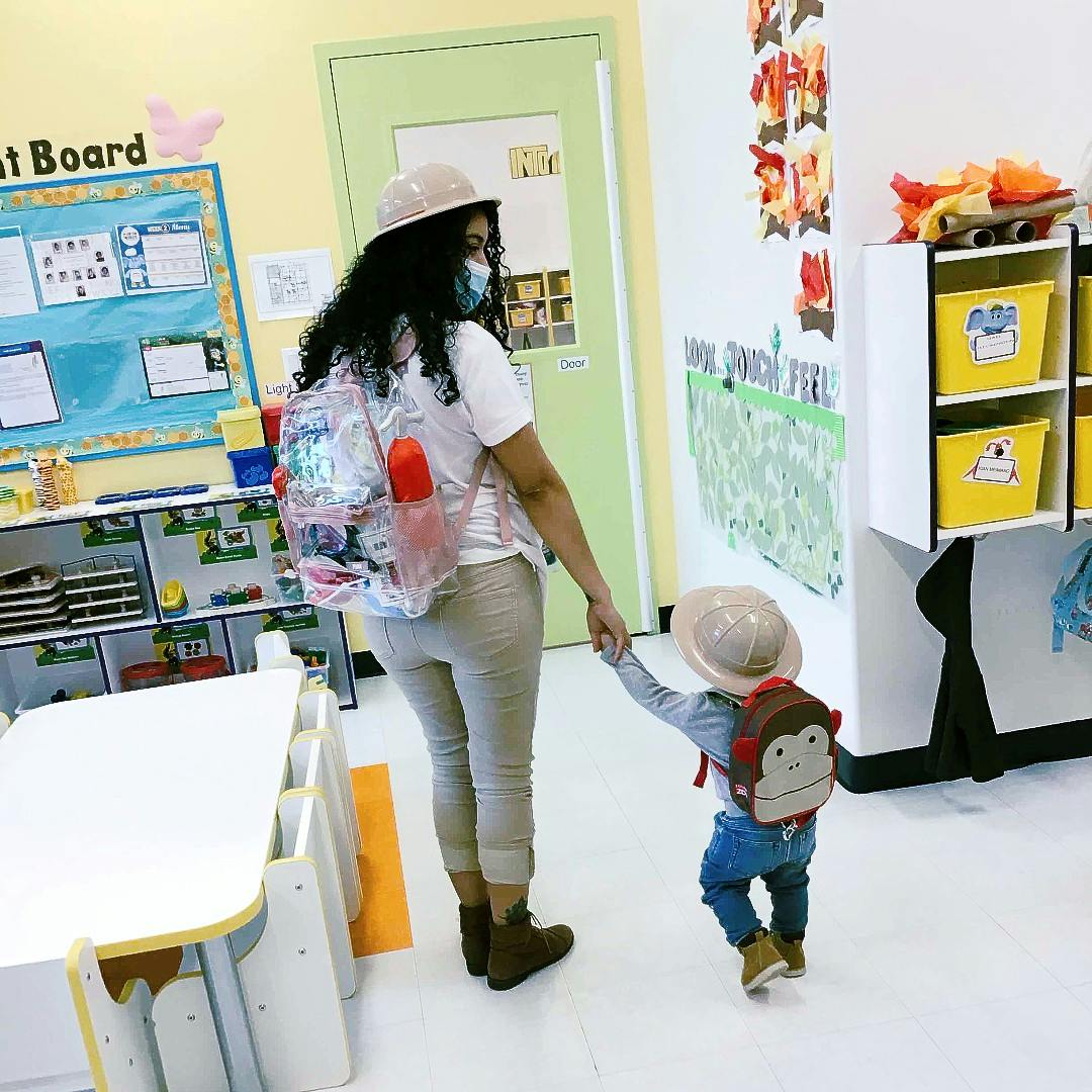 Person wearing a mask holding a child's hand in a classroom