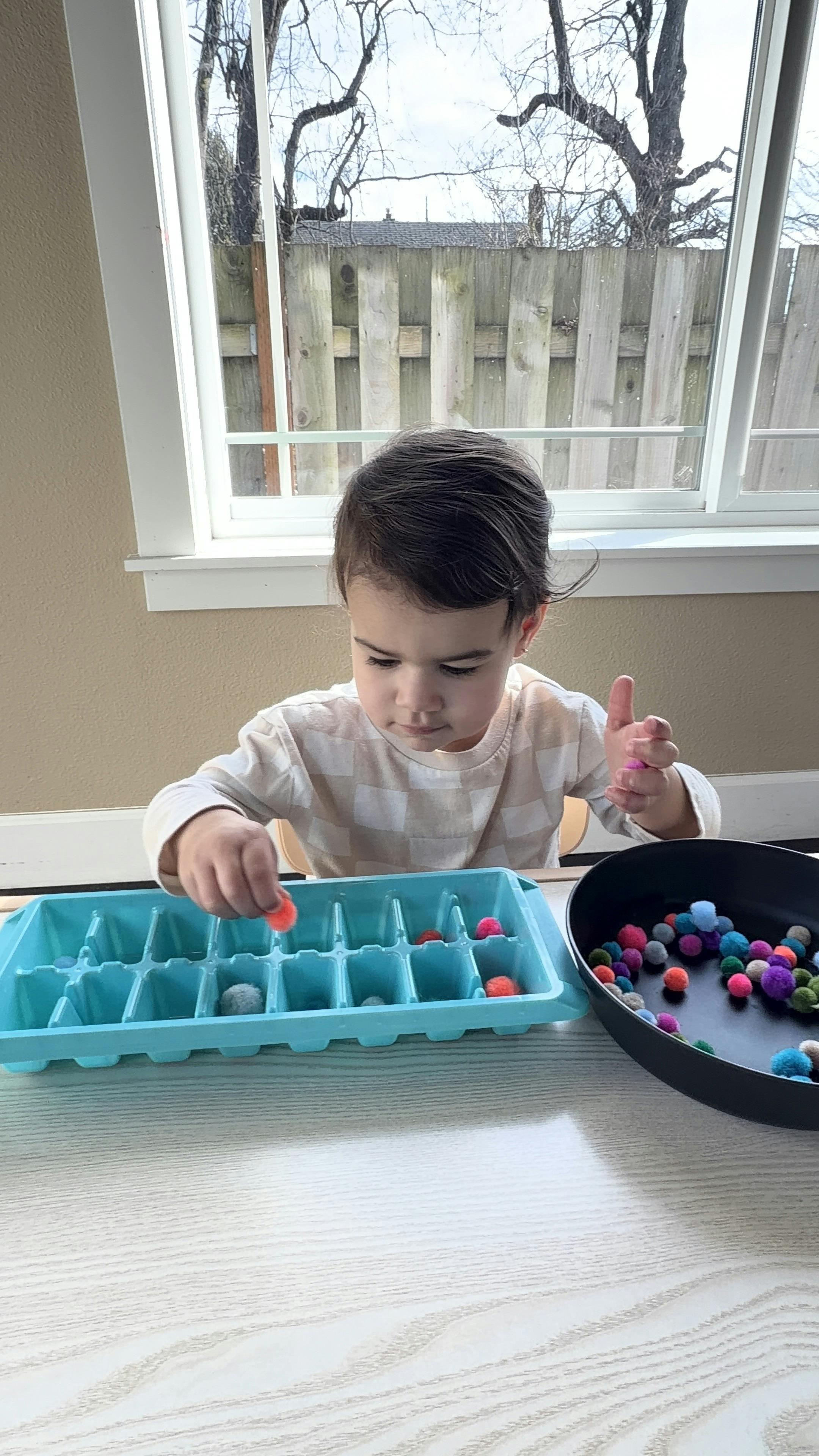 Child playing with colorful pom-poms and an ice cube tray