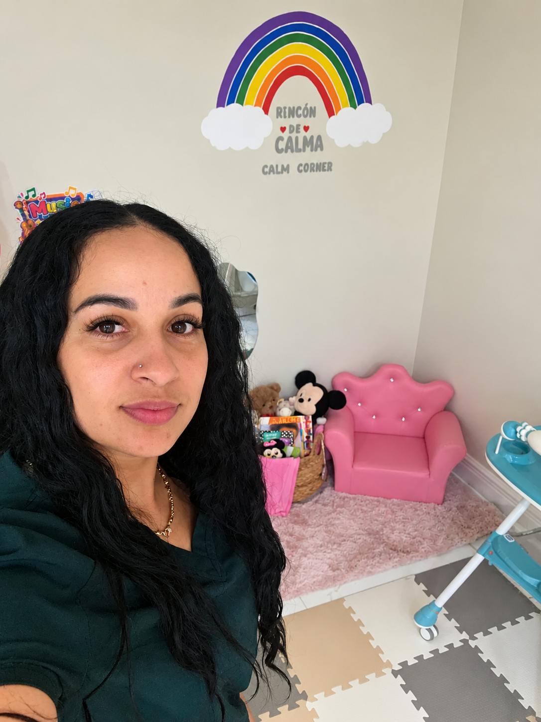 Person posing in a childs calm corner room with a pink chair and rainbow sign