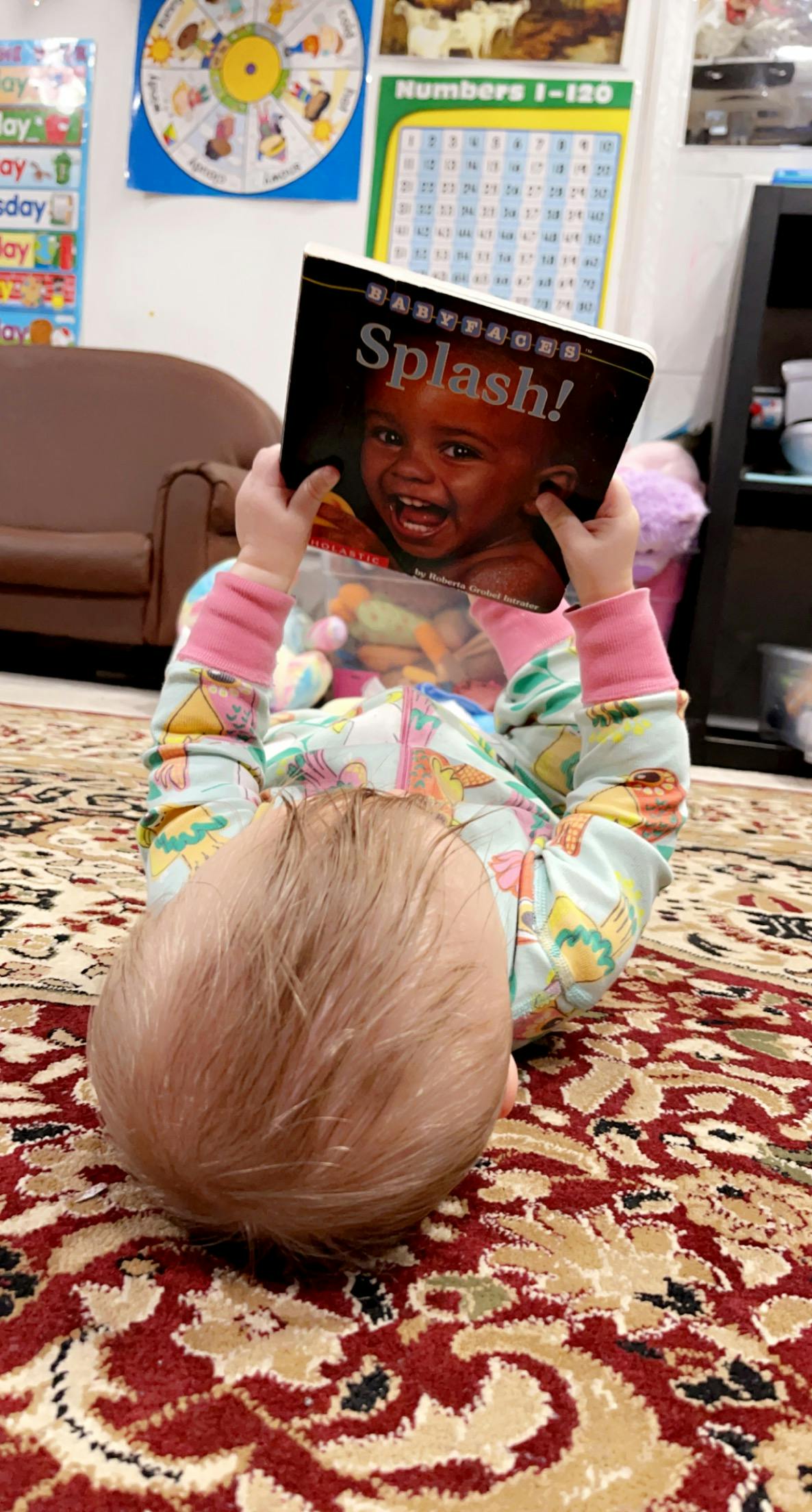 Child lying on floor holding up a book with "Splash!" on the cover