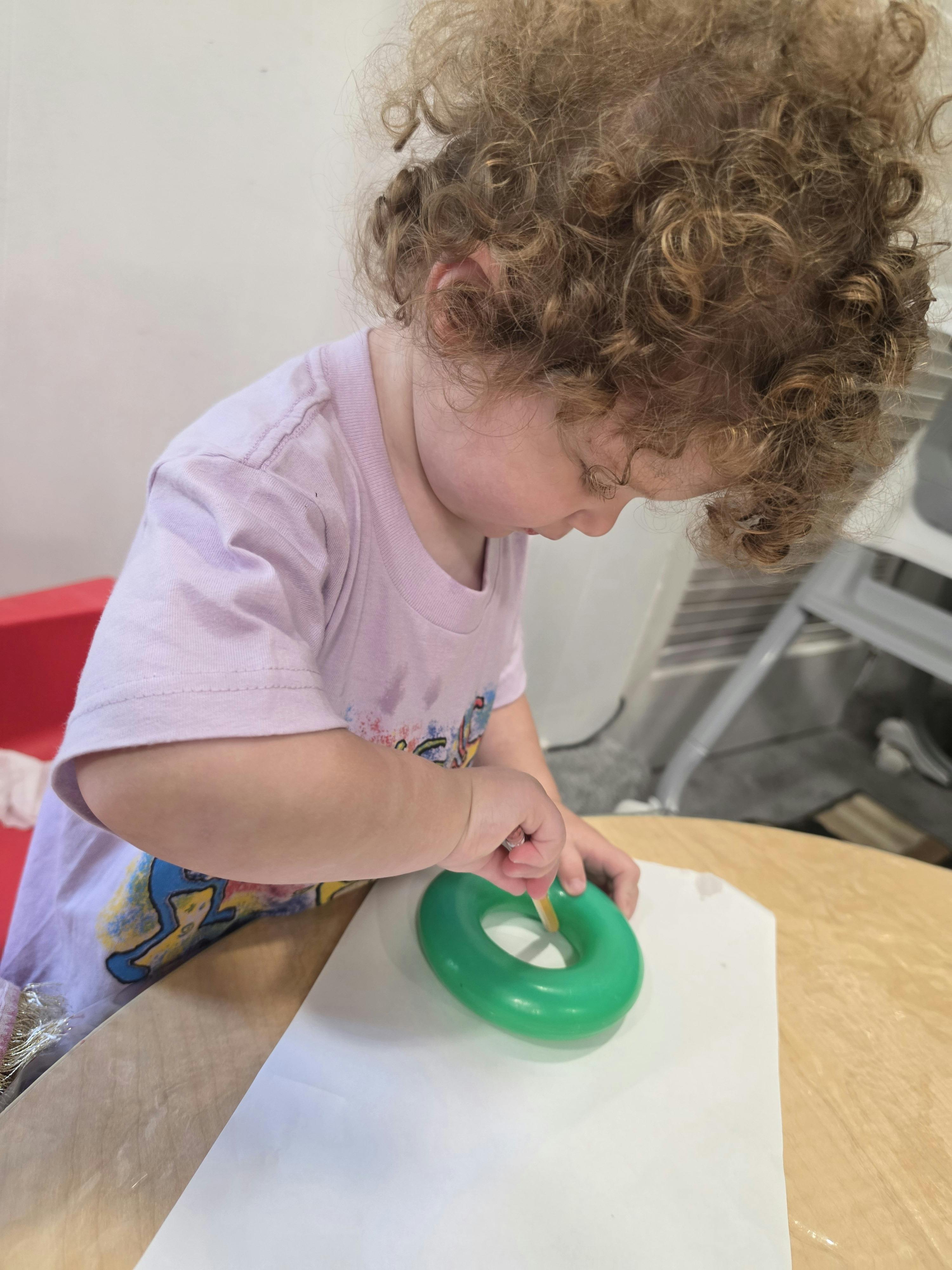 Child drawing on paper with a green donut toy