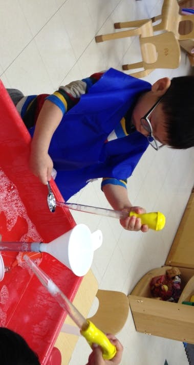 Child in glasses and blue smock playing with water and toys