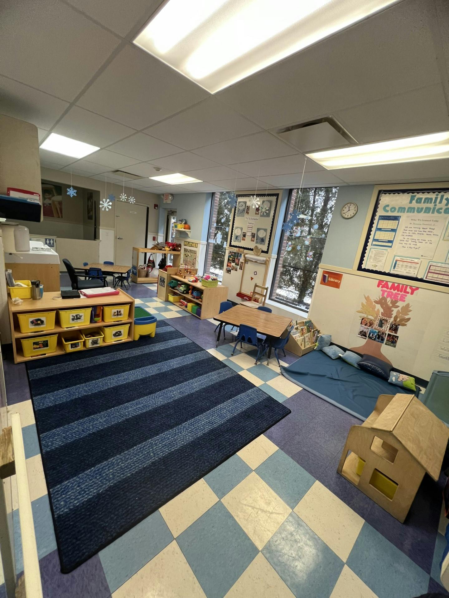Classroom with child-sized tables, storage bins, and a rug on blue and white tiled floor