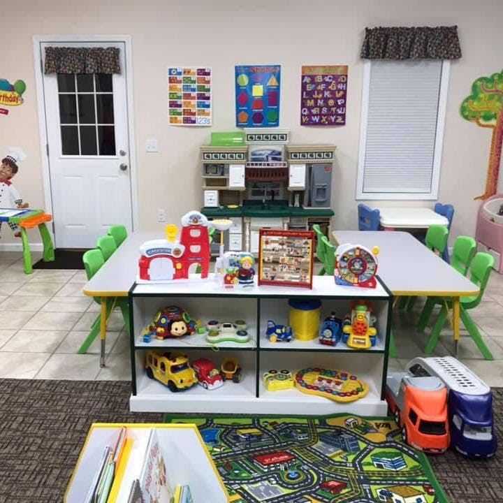 Playroom with tables, chairs, shelves of toys, and a child in the background