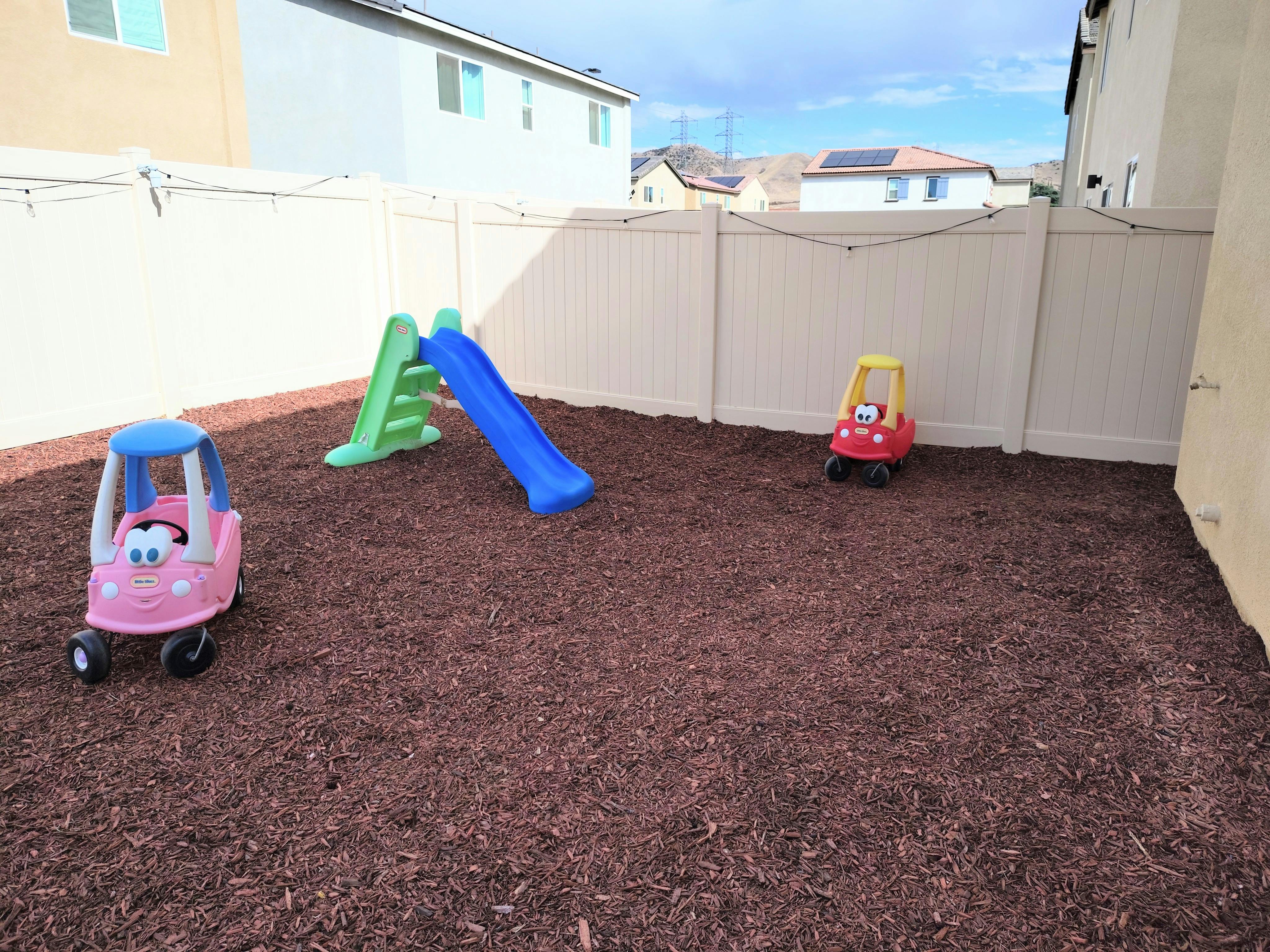 Two toy cars and a slide on a wood chip ground