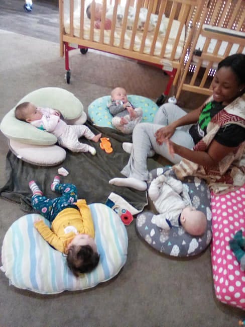Person sitting on floor with multiple babies on pillows
