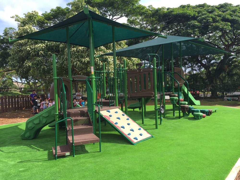 Playground with green slides, climbing wall, and artificial turf