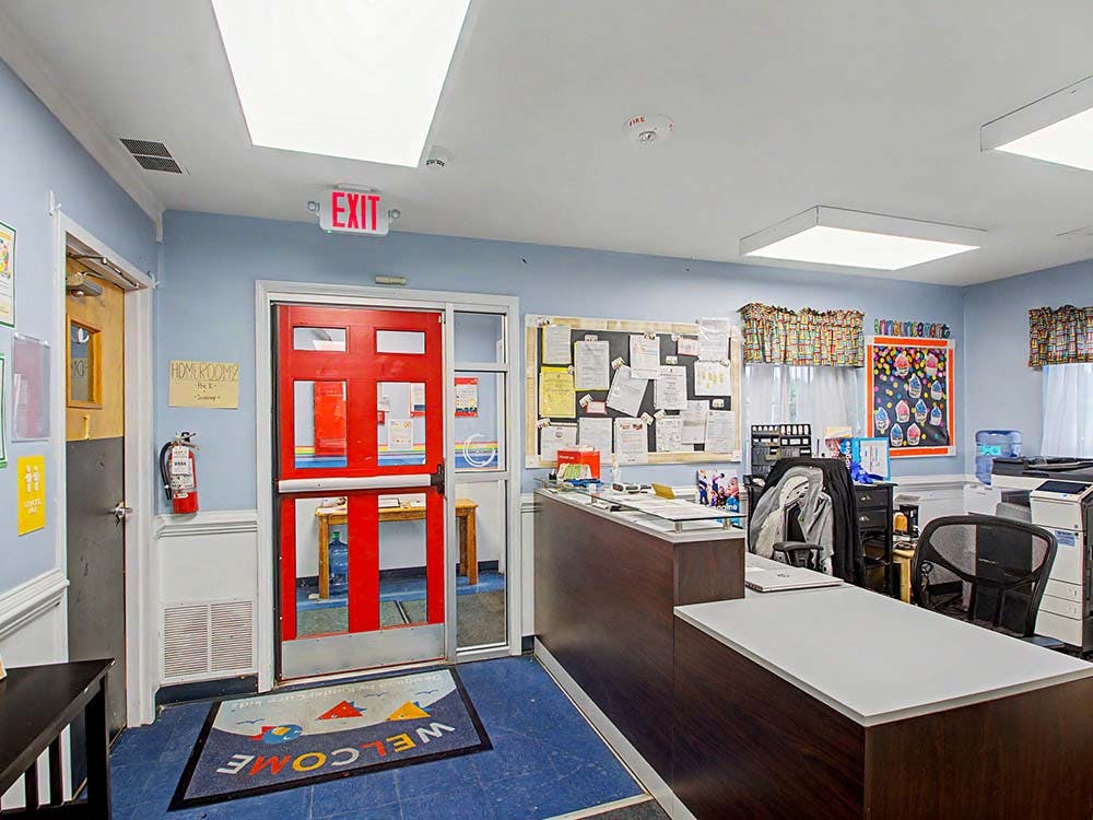 Reception area in a school with a red exit door and "WELCOME" doormat