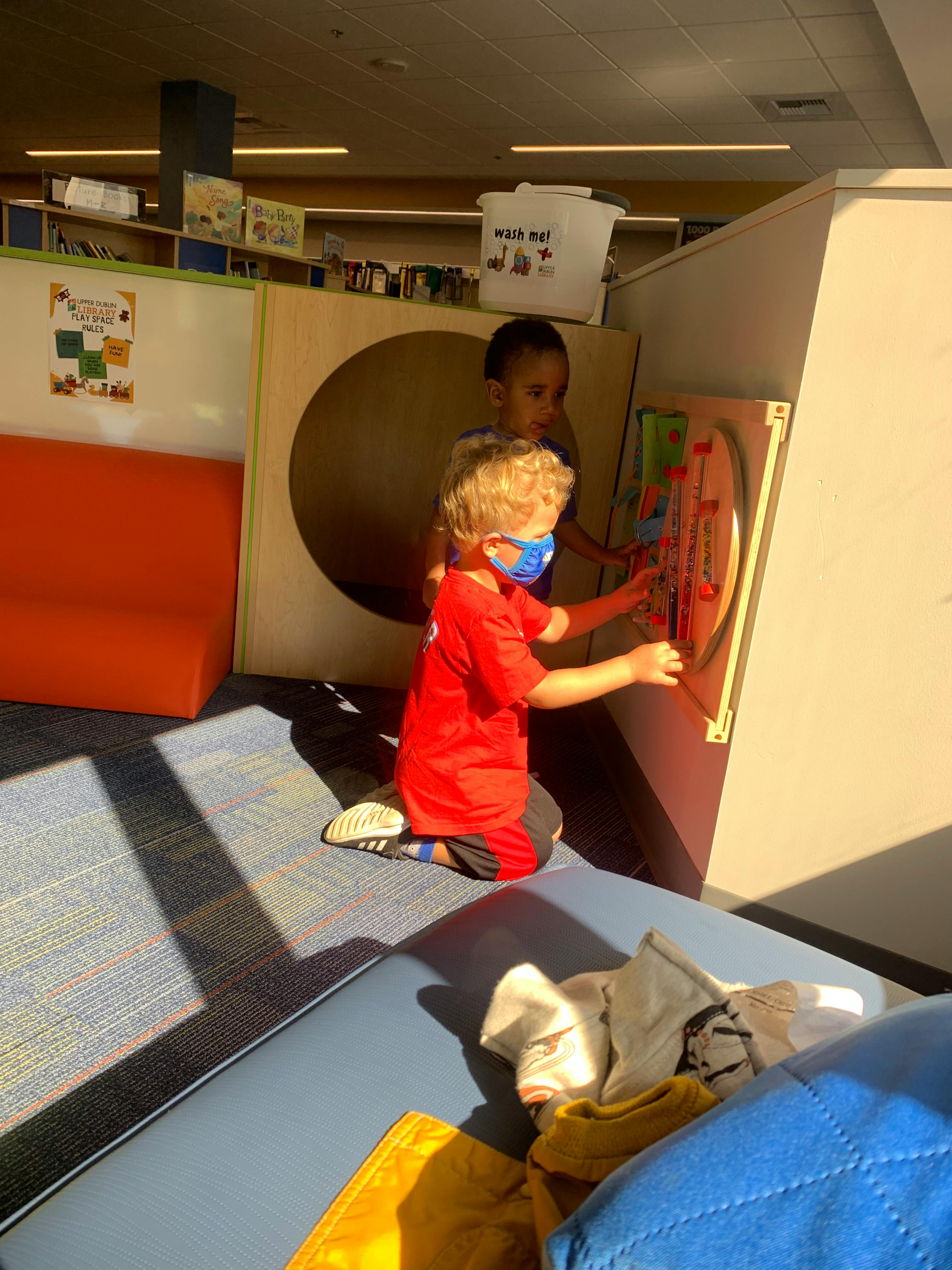 Child in a mask playing with a wall-mounted activity, another child behind