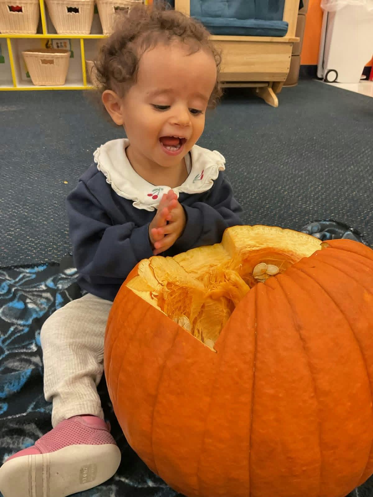Child sitting on the floor next to a carved pumpkin