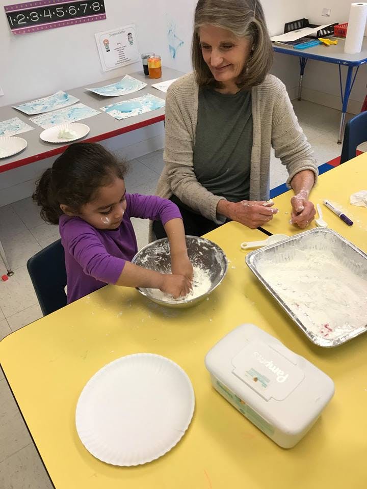 Adult and child mixing ingredients in bowls atable in a classroom