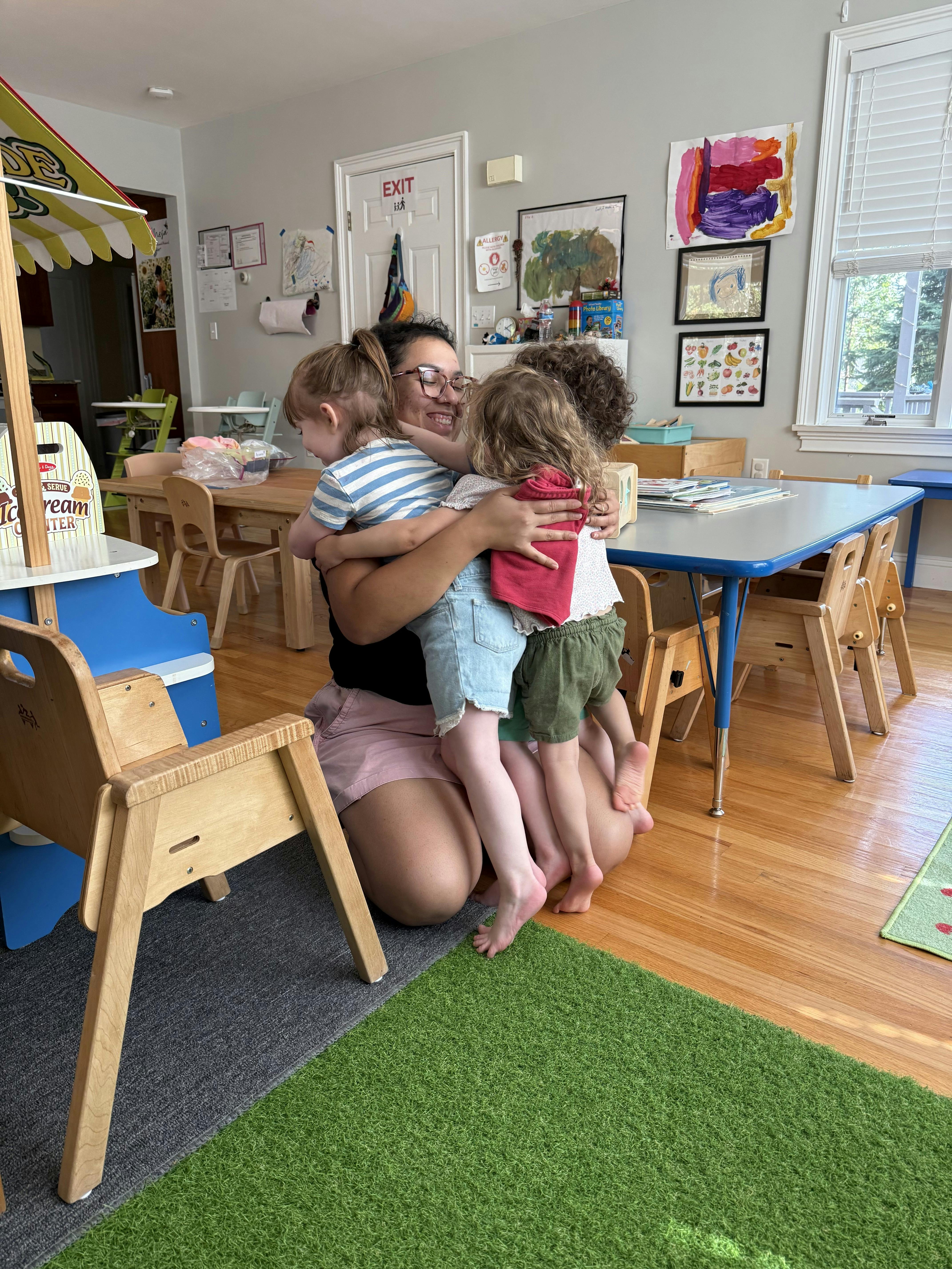 Person kneeling and hugging three children in a classroom
