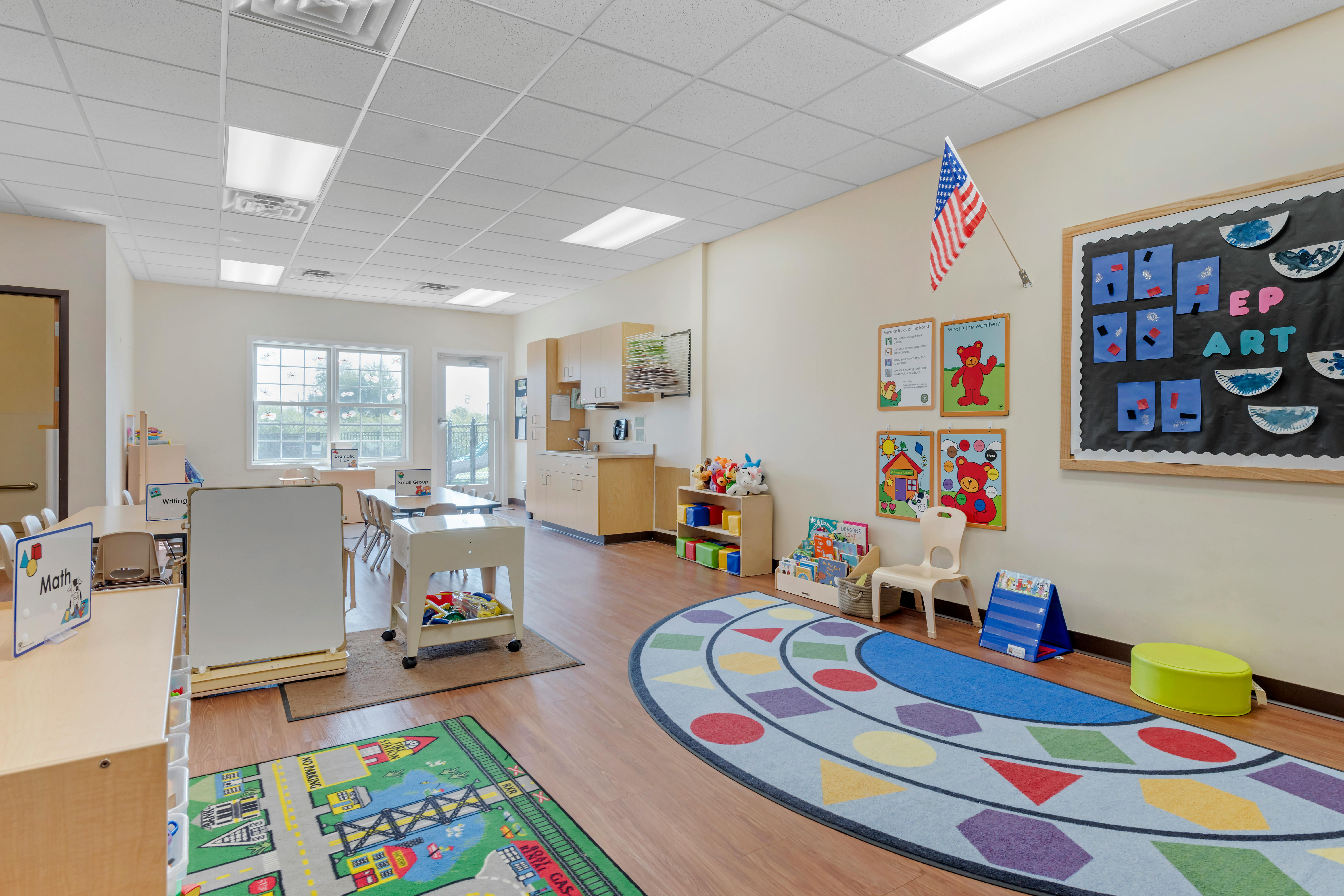 Classroom with tables, chairs, a play kitchen, and a colorful rug