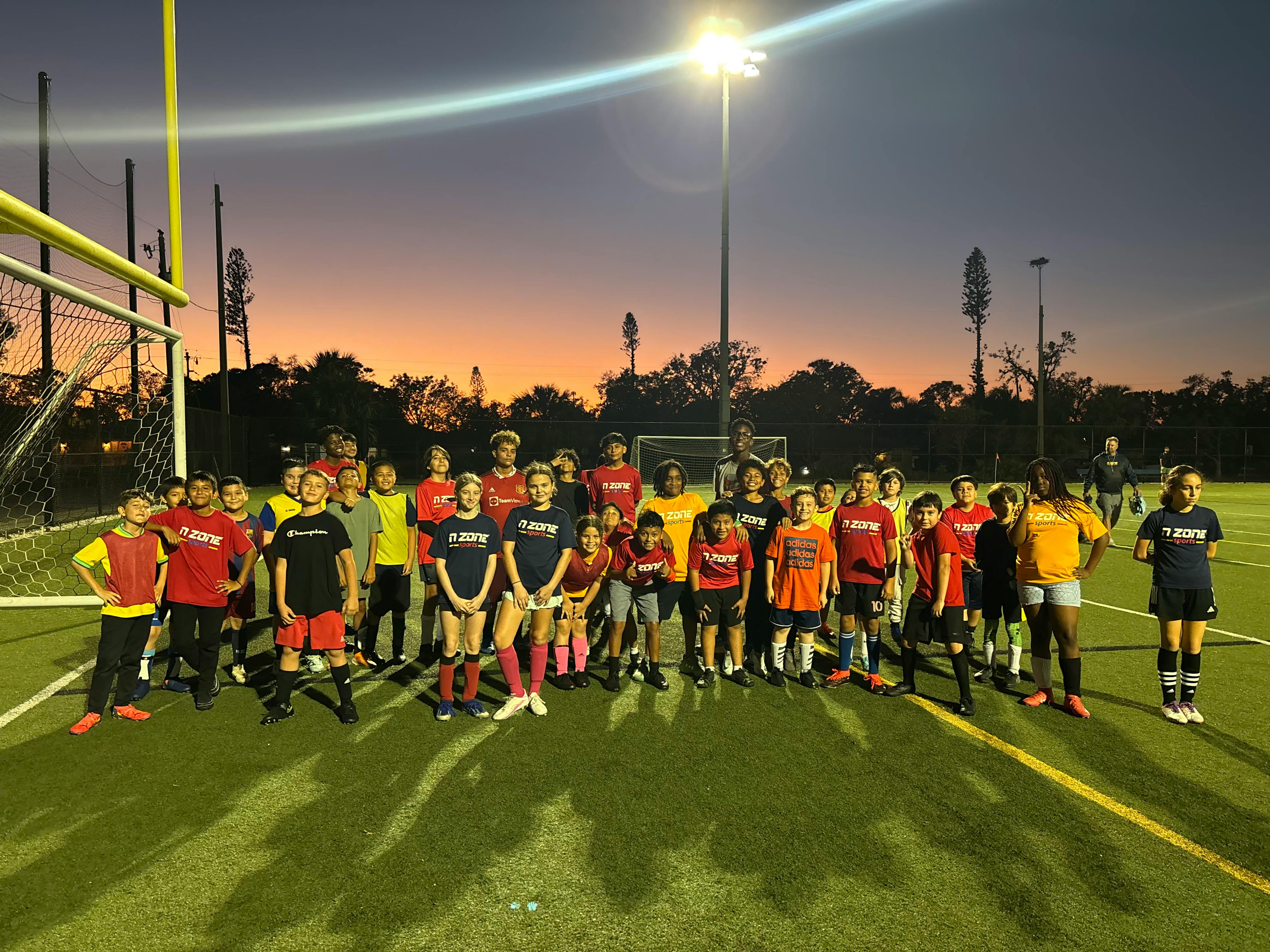 Group of people in athletic wear standing on a sports field at dusk