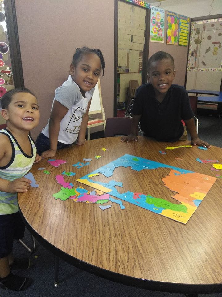 Three children standing around a table with a colorful puzzle