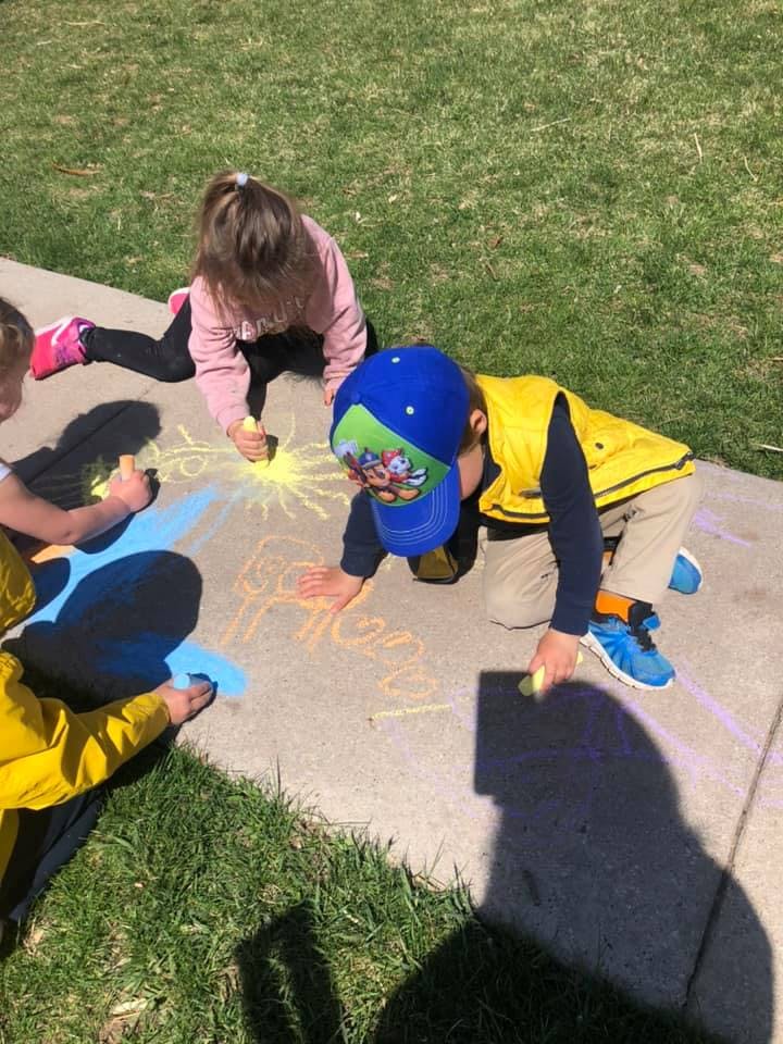 Three children drawing with chalk on a sidewalk