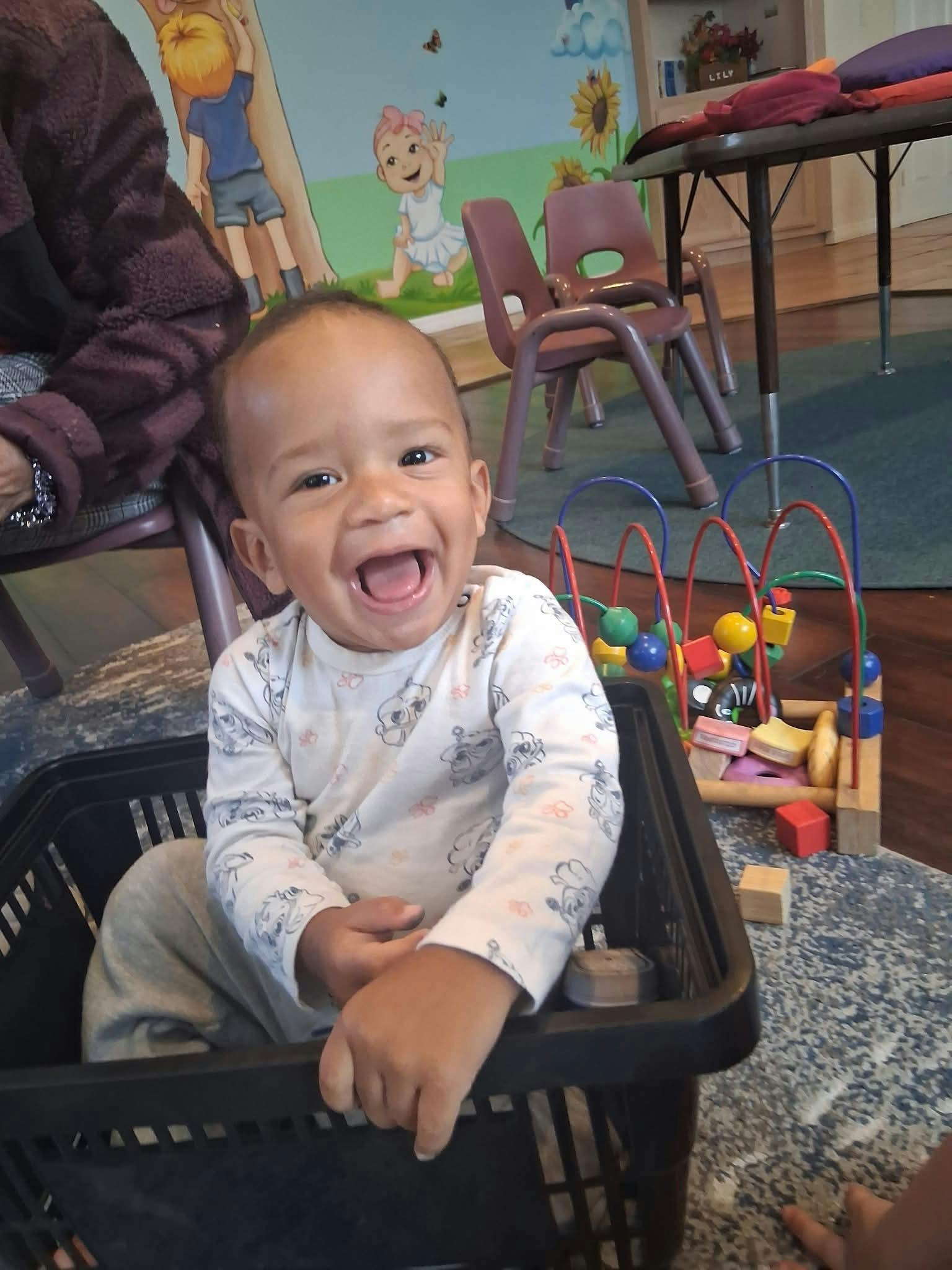 Smiling child sitting in a black plastic basket in a playroom