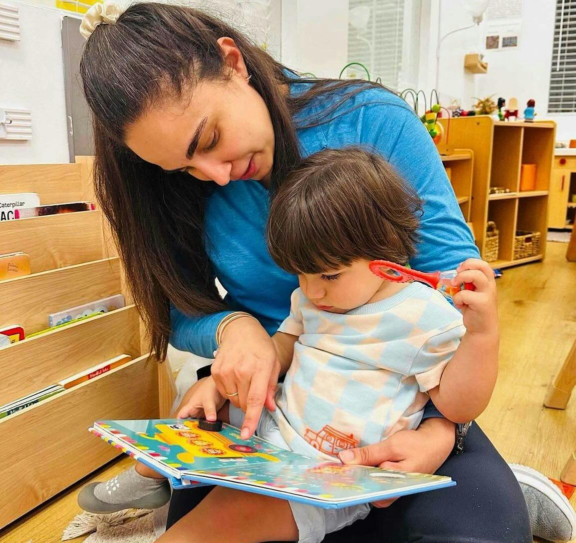Person and child reading a book together in a classroom