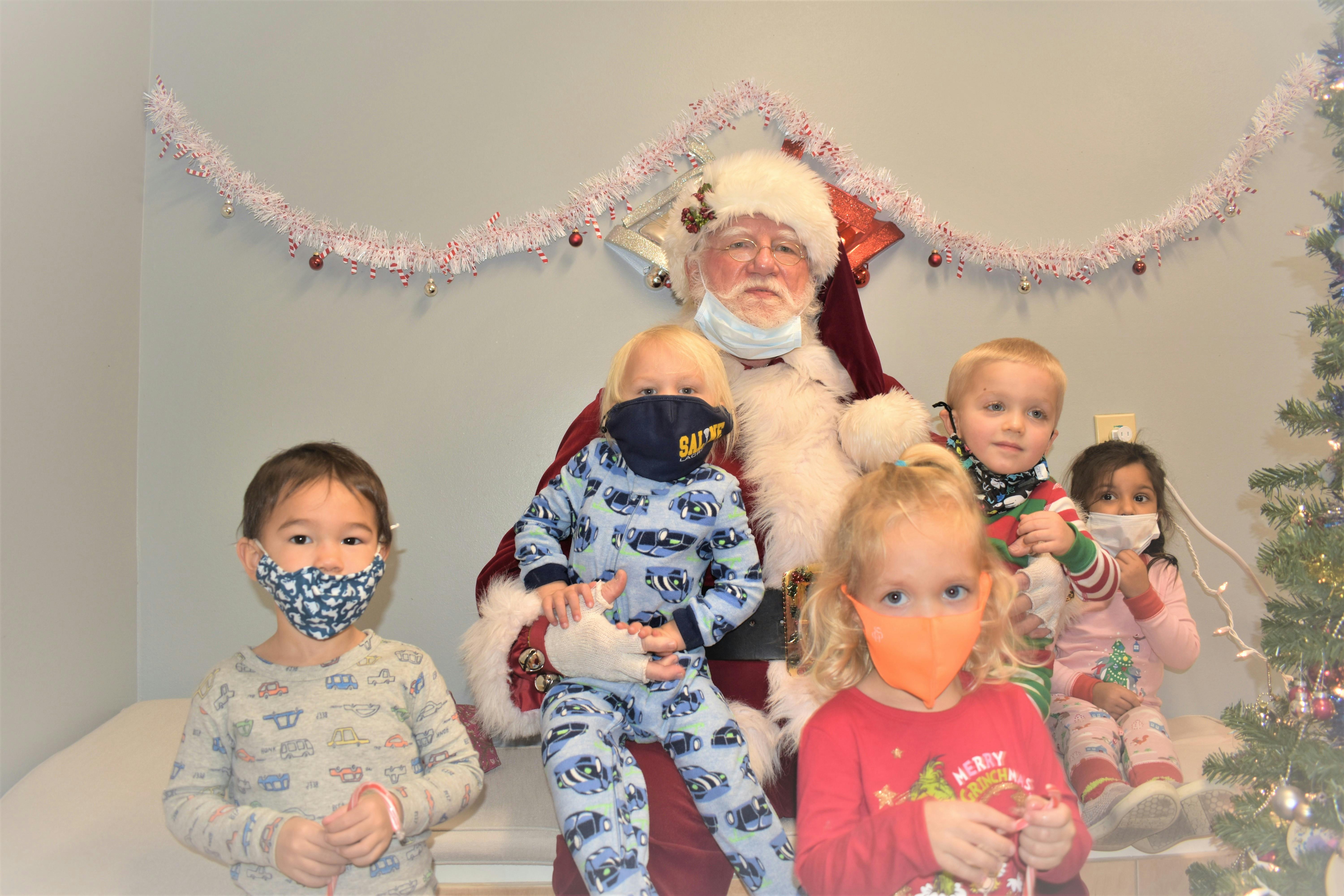 Person dressed as Santa Claus with four children wearing face masks
