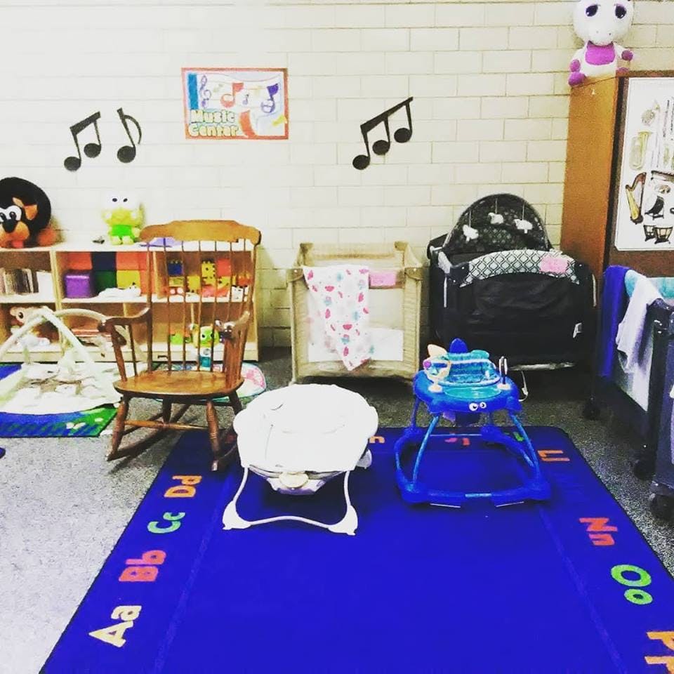 Childcare room with cribs, playpen, baby walker, and alphabet rug