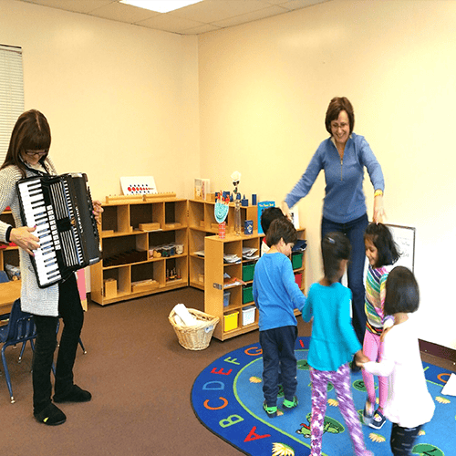 Person playing accordion while another person interacts with children in a classroom