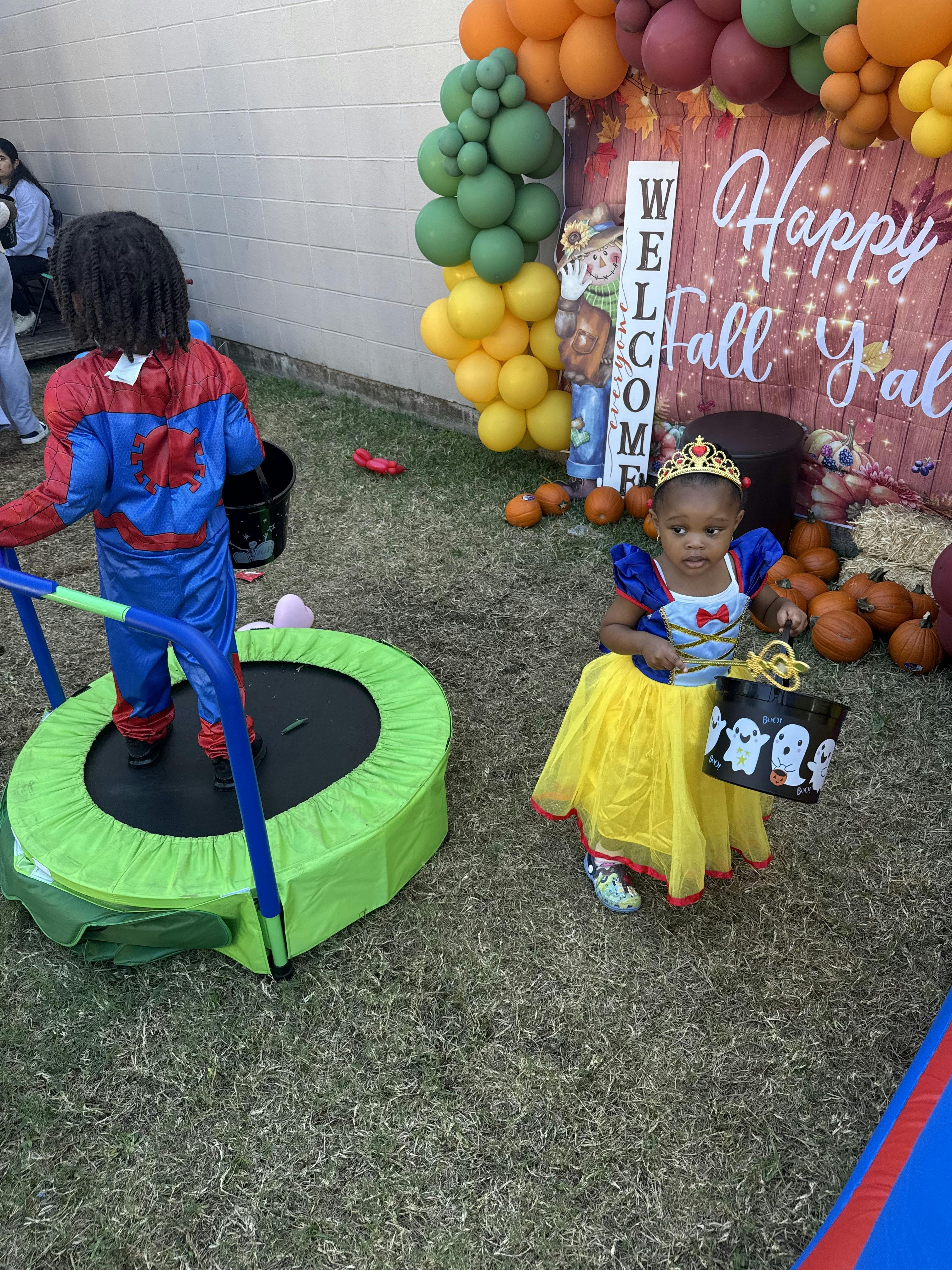 Child in Spider-Man costume on trampoline, child in Snow White costume holding bucket