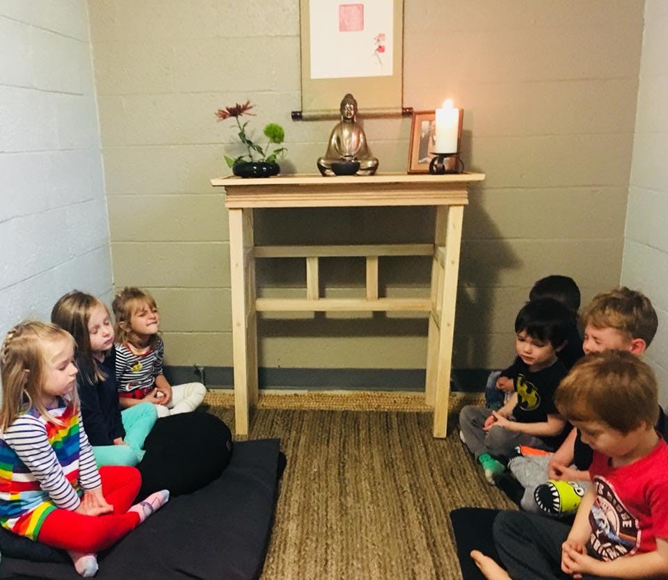 Children sitting on floor in front of a small table with a statue and candle