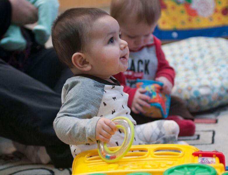 Child playing with a yellow toy, another child in the background