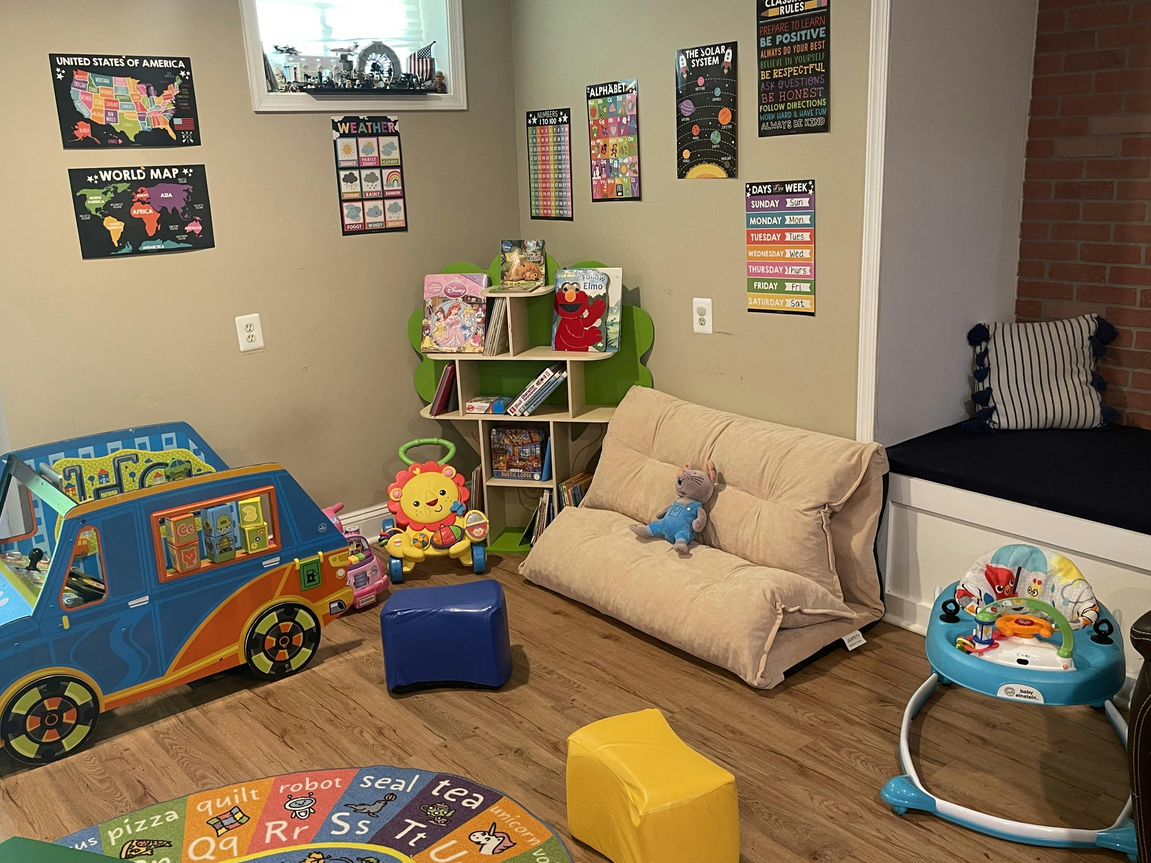Playroom with educational posters, toy van, small folding sofa, and baby toys