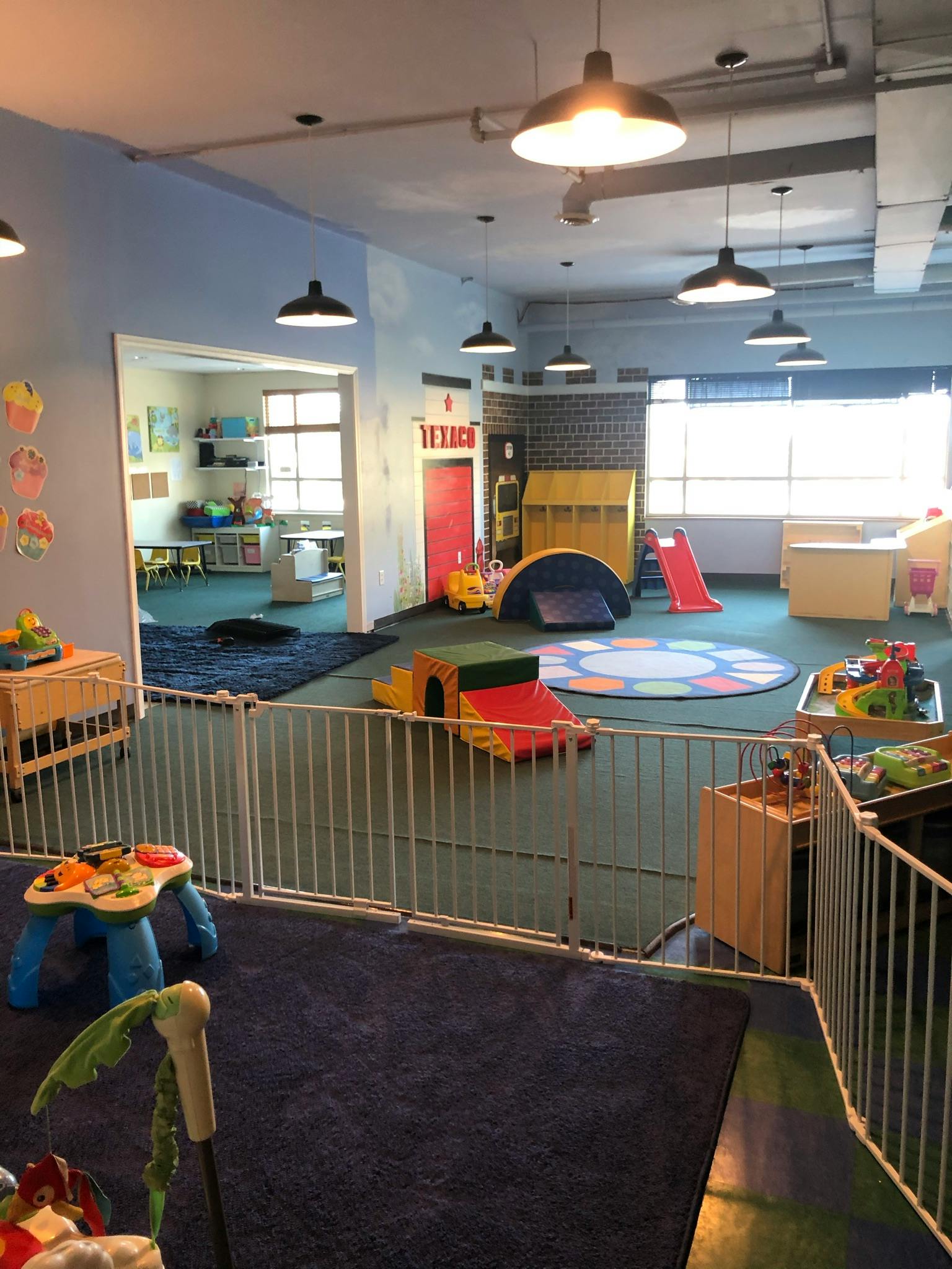 Indoor play area with various toys and equipment, separated by a white fence