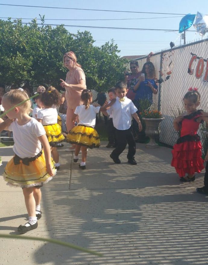 Children in costumes dancing outdoors with an adult supervising