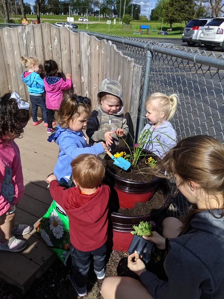 Children and an adult planting in red pots outdoors