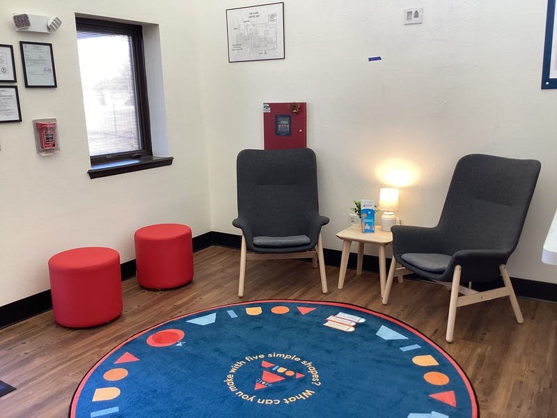 Waiting area with two lounge chairs, two red cylindrical ottomans, and a round rug