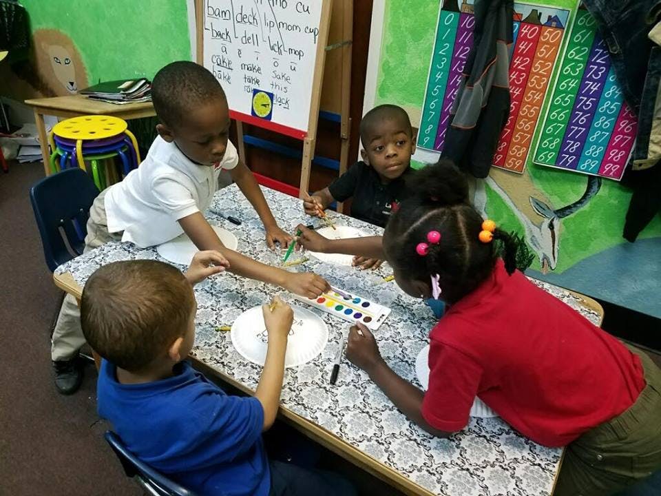 Four children painting at a table in a classroom